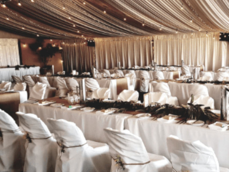 Elegant event tent decorated with string lights, white drapery, and round tables with white chair covers.