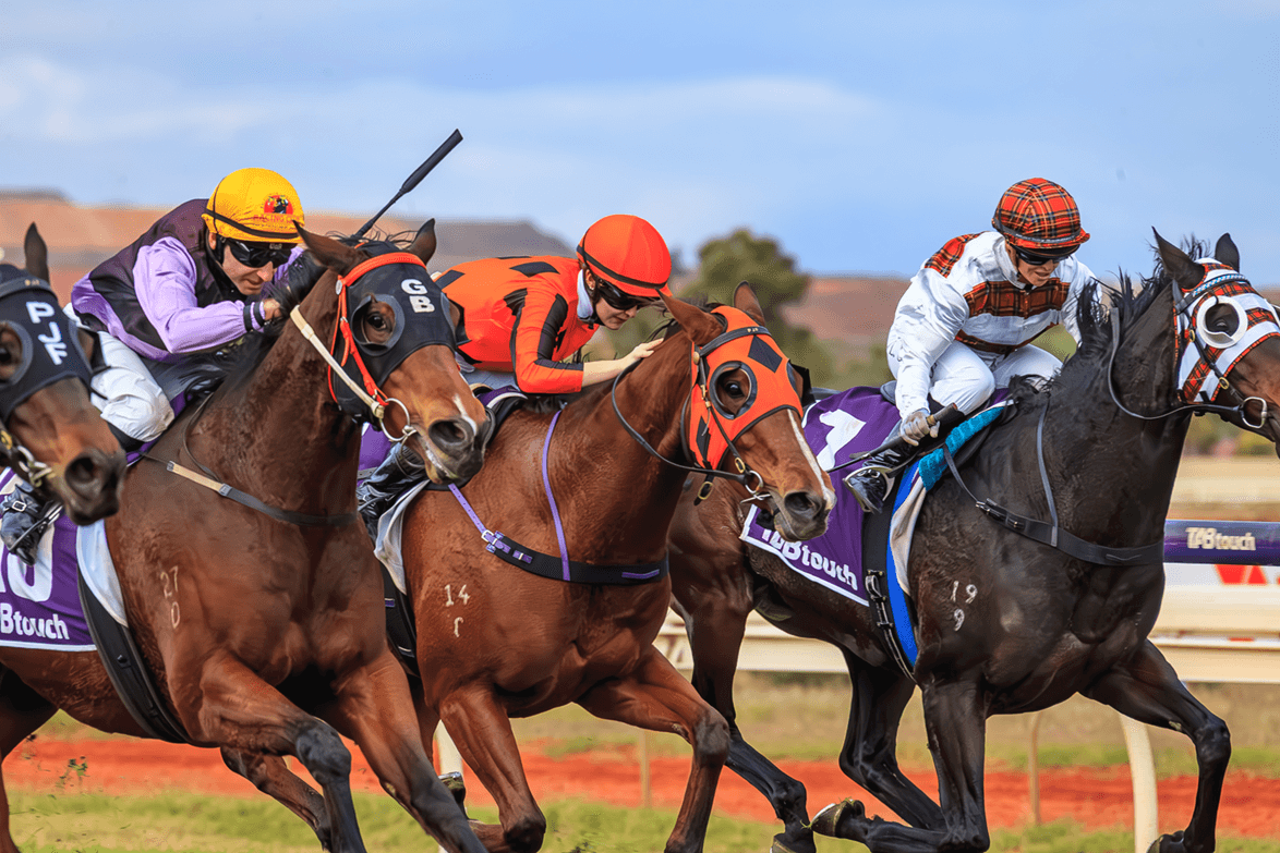 Jockeys riding horses in a horse race, wearing colorful helmets and riding gear, on a race track with a clear blue sky in the background.