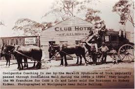 Historical black and white photo of a horse-drawn coach outside the Club Hotel, with trees and a building in the background.