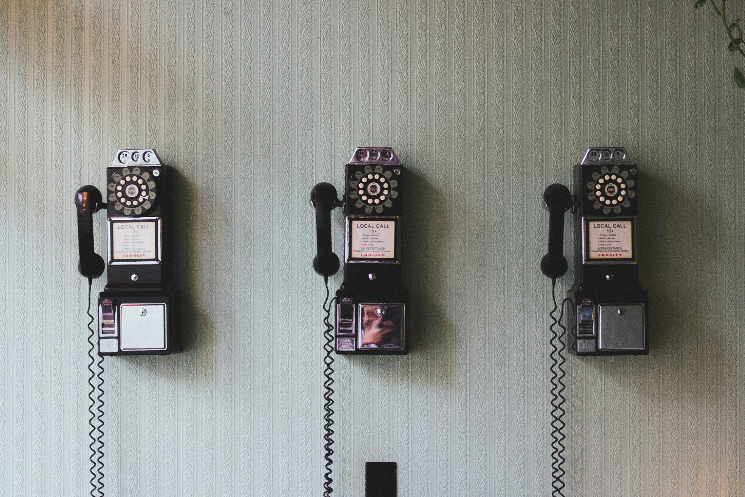 Three vintage black payphones mounted on a light-colored patterned wall.