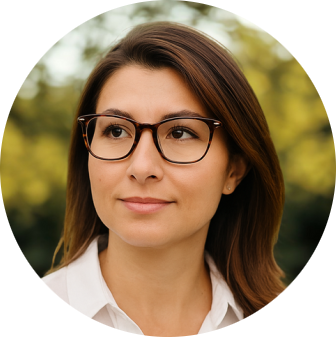 A woman with shoulder-length brown hair and glasses looking to the side outdoors.
