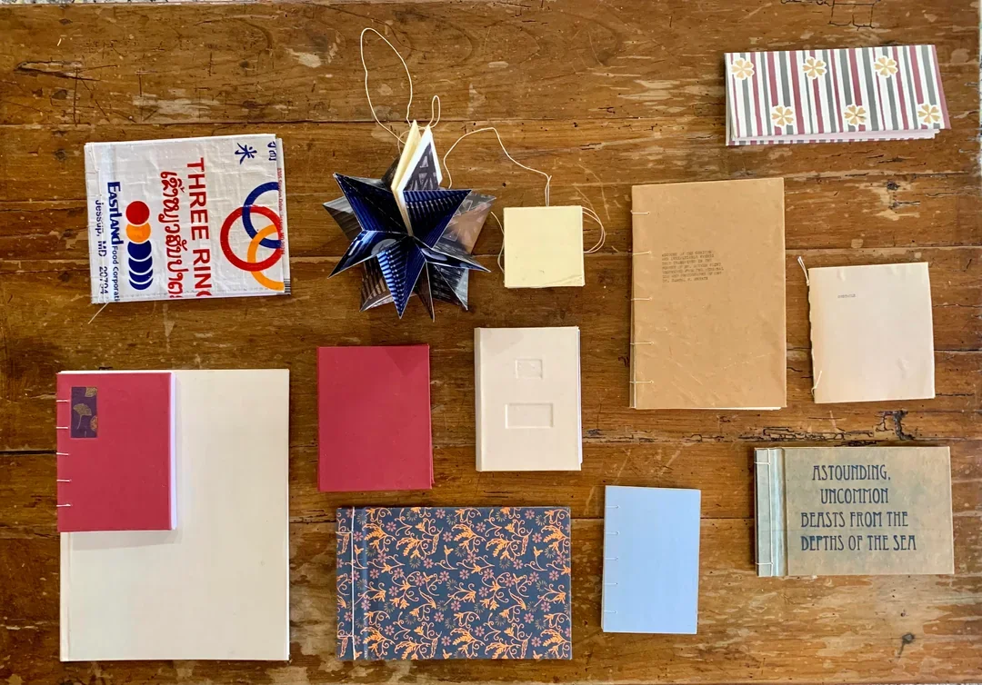 Various folded paper objects, including books, cards, and paper crafts, arranged on a wooden surface.
