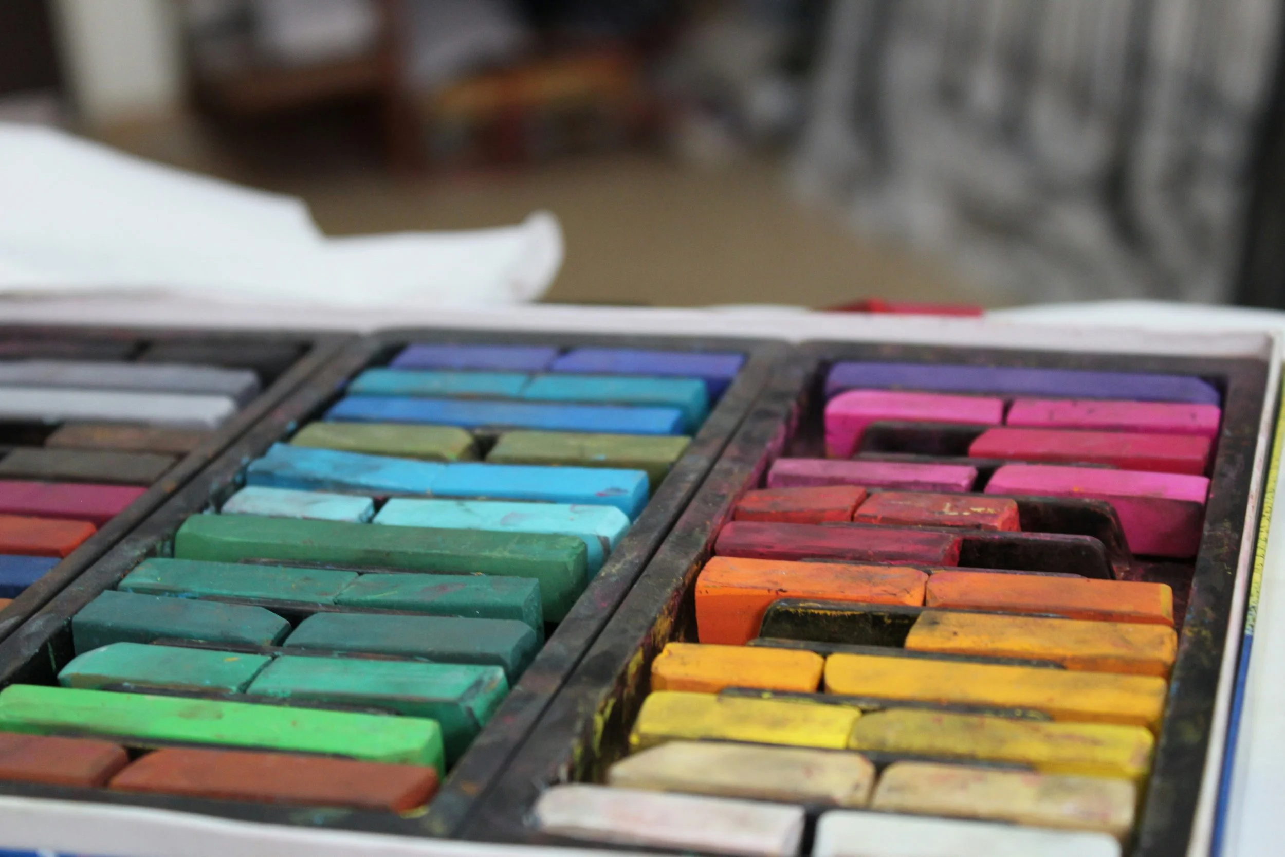 A set of colorful pastels in a plastic case, arranged in sections with shades of blue, green, pink, purple, orange, yellow, and white.