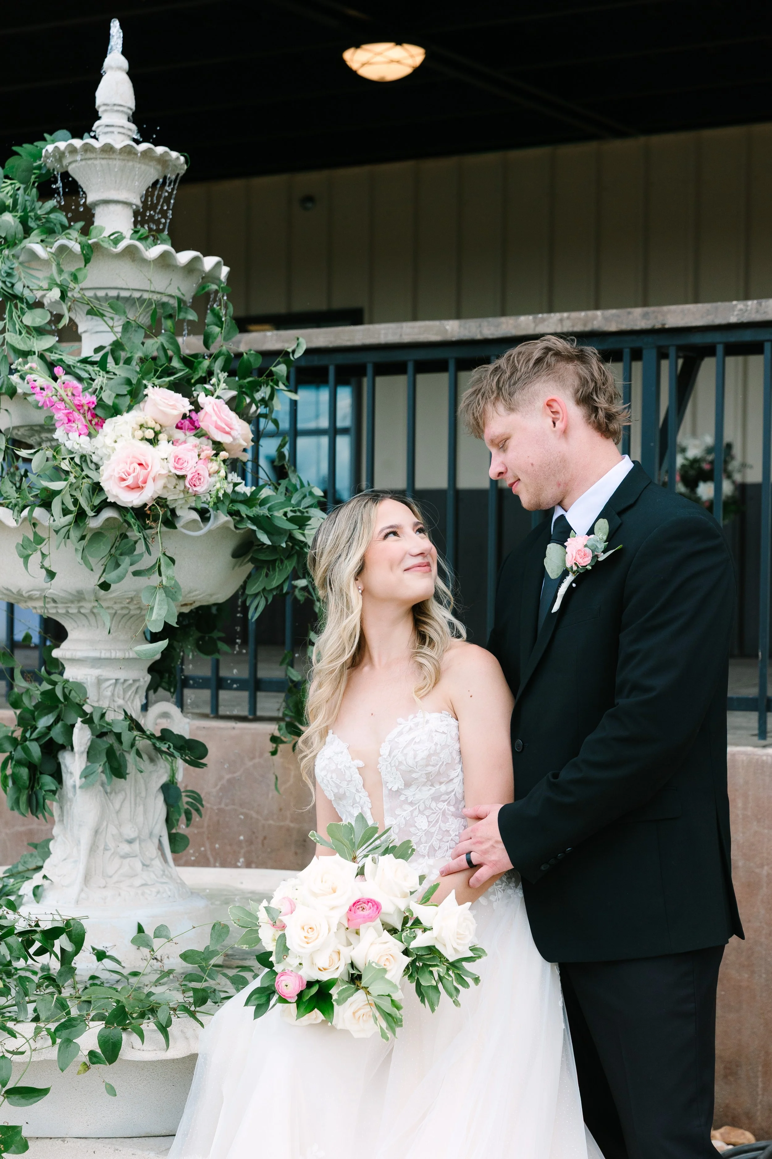 Bride and groom posing by a tiered stone fountain adorned with lush pink and white floral decor designed by Ignited Events in Dallas Fort Worth