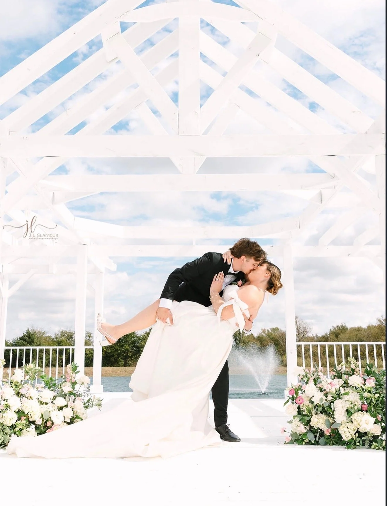 Groom dipping and kissing bride under a white outdoor pavilion framed by floral decor and a fountain at a Dallas Fort Worth, Texas wedding planned and designed by Ignited Events