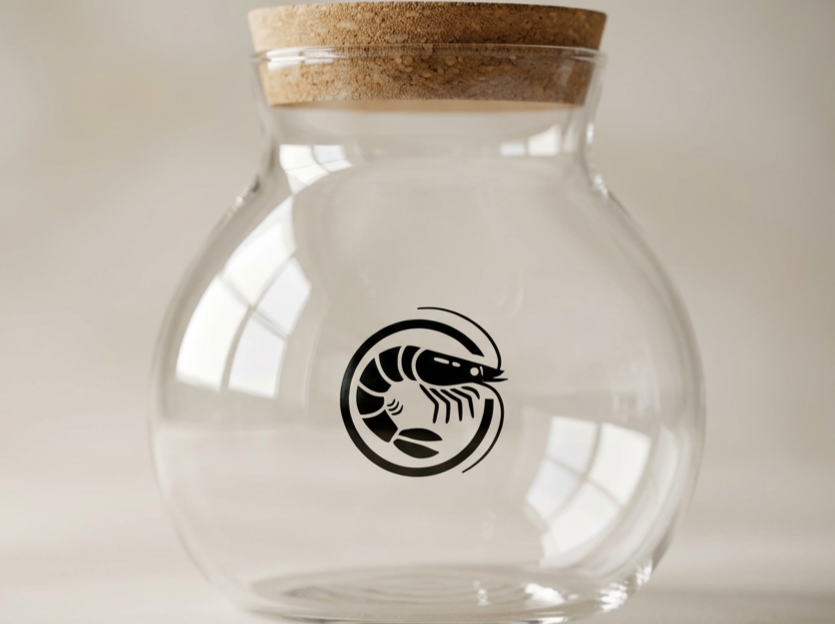 Clear glass jar with a cork lid and a black crustacean logo on the front, set against a light background.