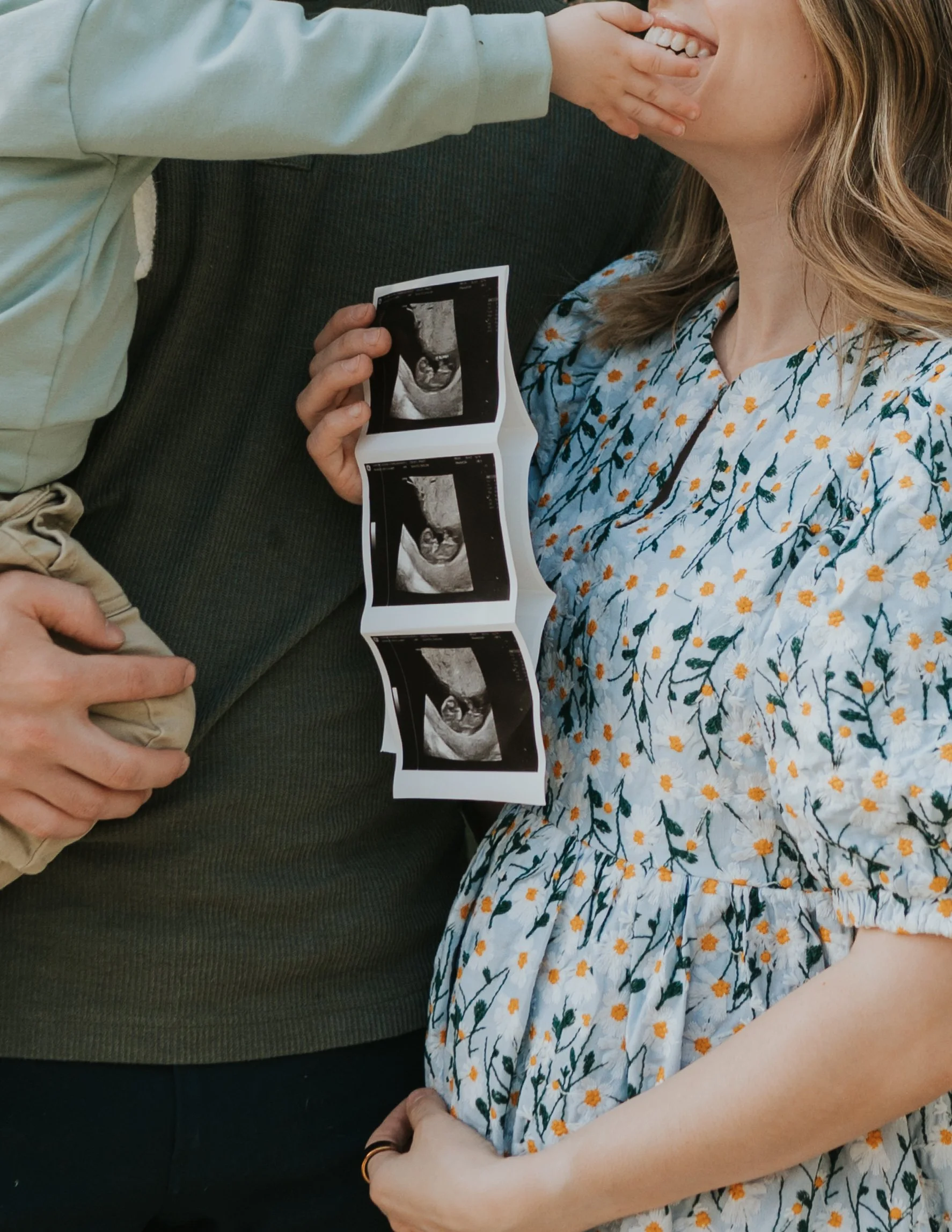 close up of ultrasound with toddler hand and mom and dad hands in picture