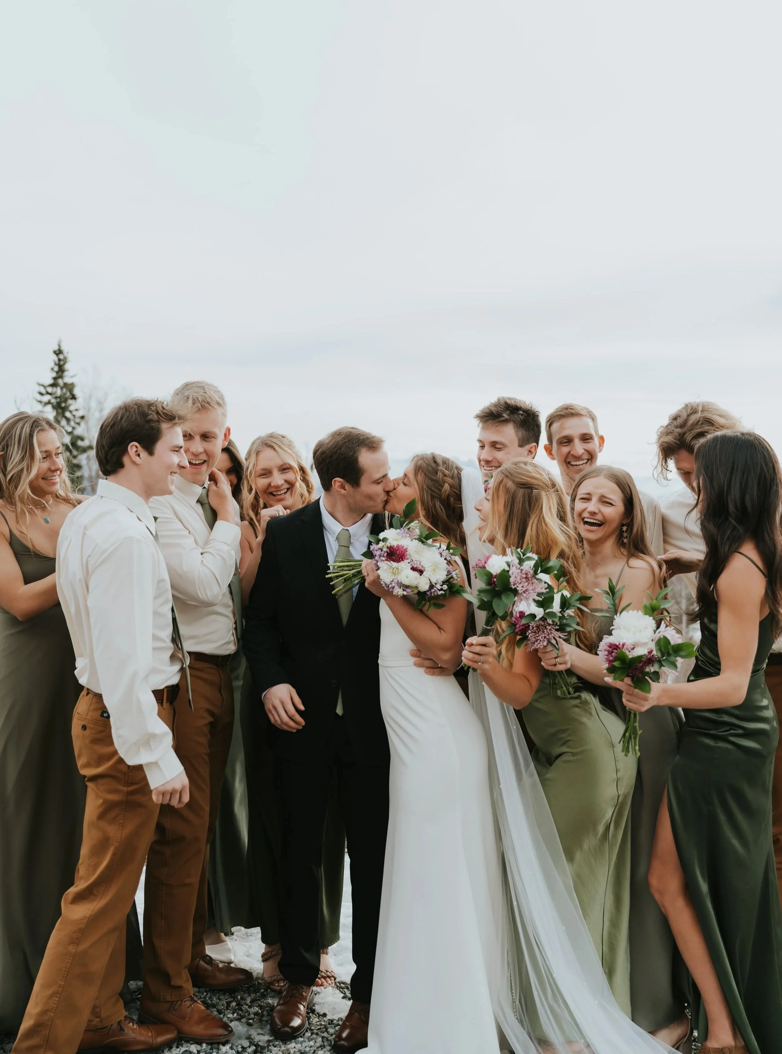 wedding party surrounds newlywed couple kissing