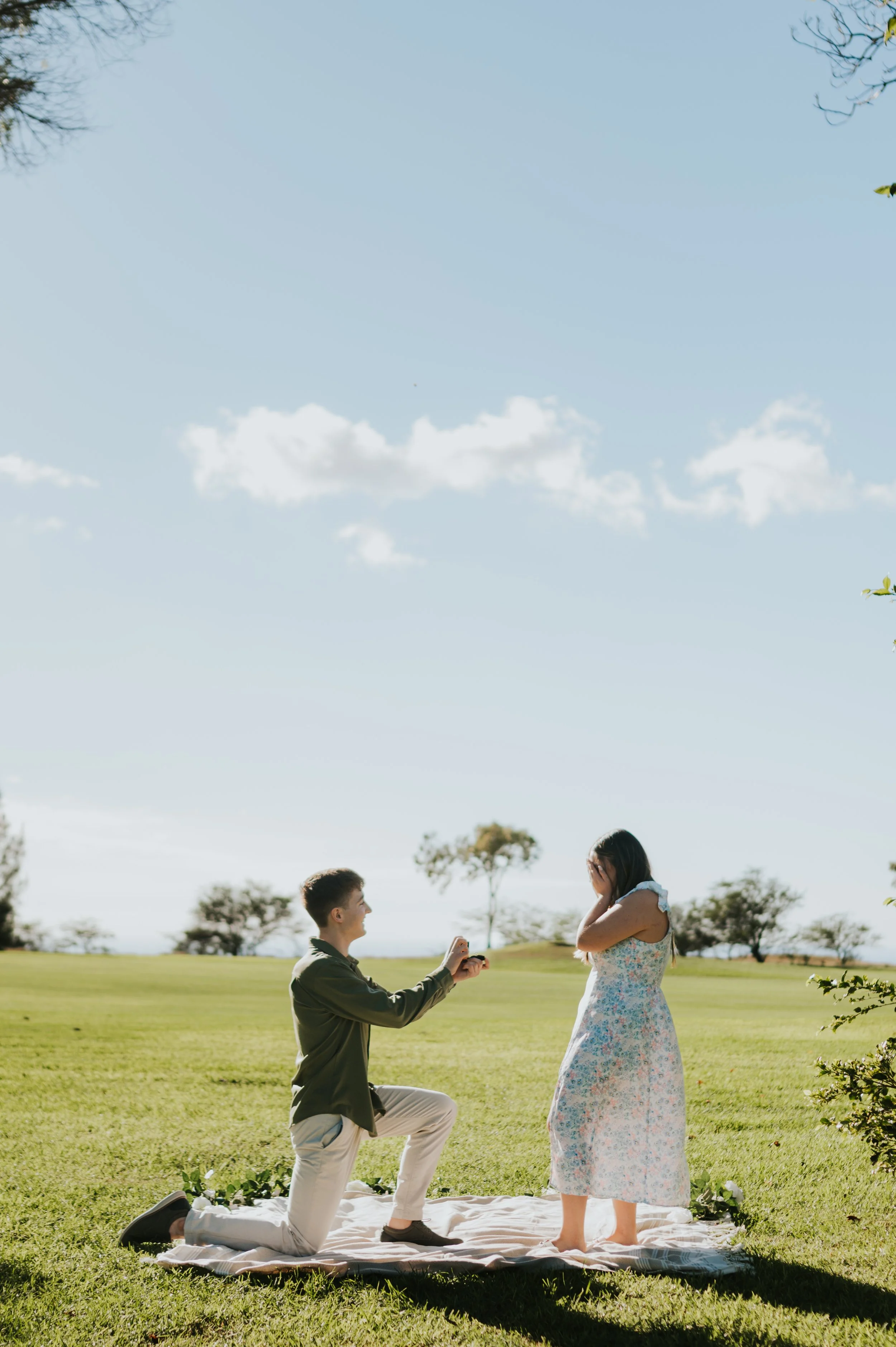 man kneeling on ground in green field with ring in front of surprised woman