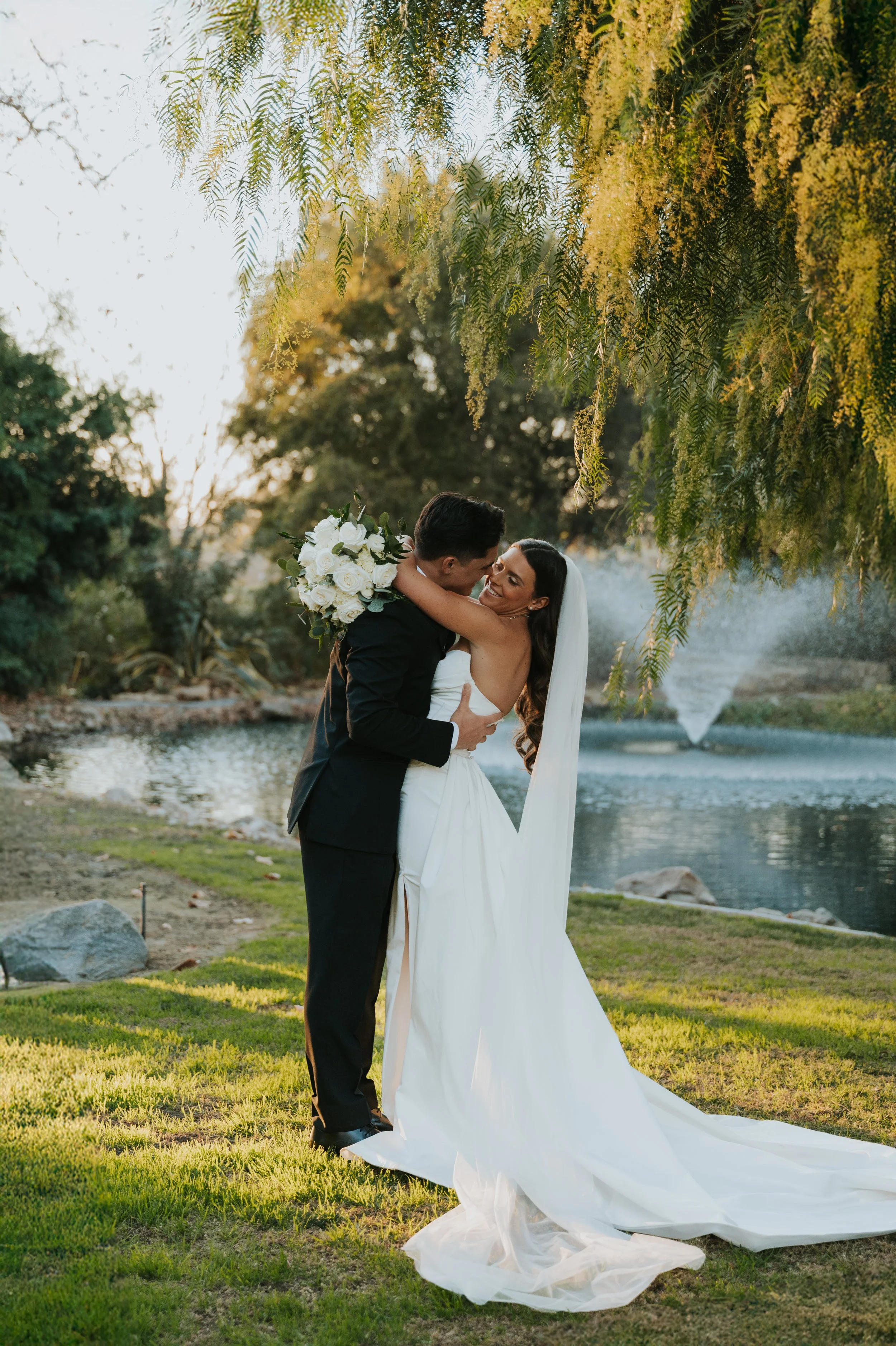 couple smiling at each other in wedding attire in front of lake