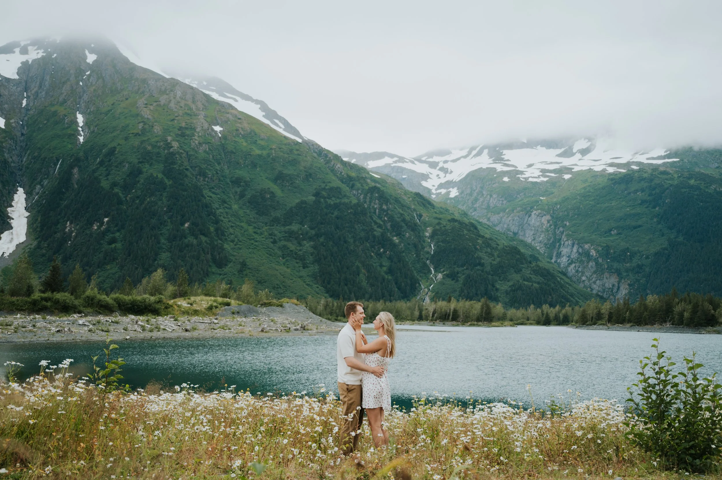 engaged couple in front of alpine lake smiling