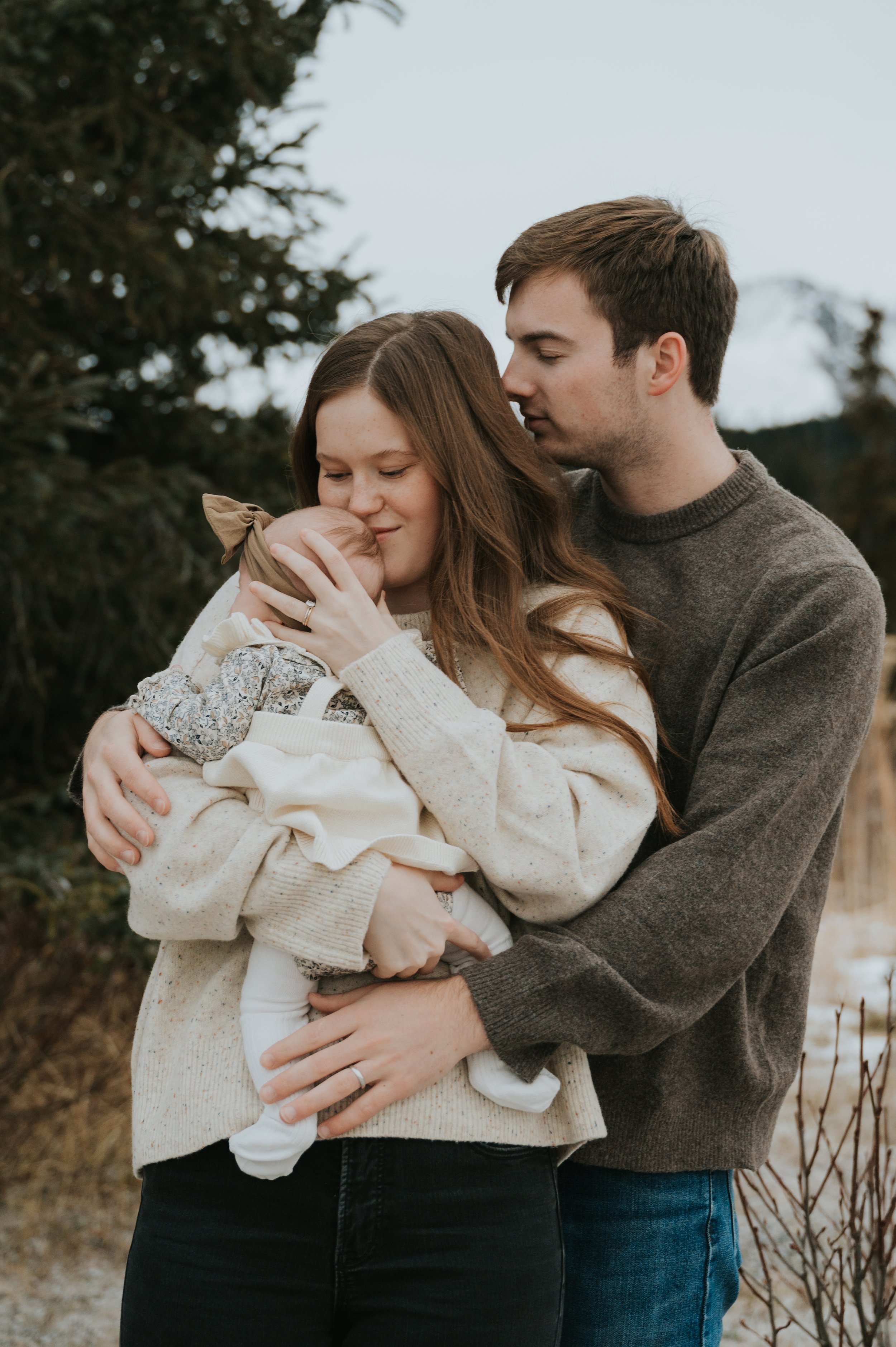 parents snuggling newborn outdoors