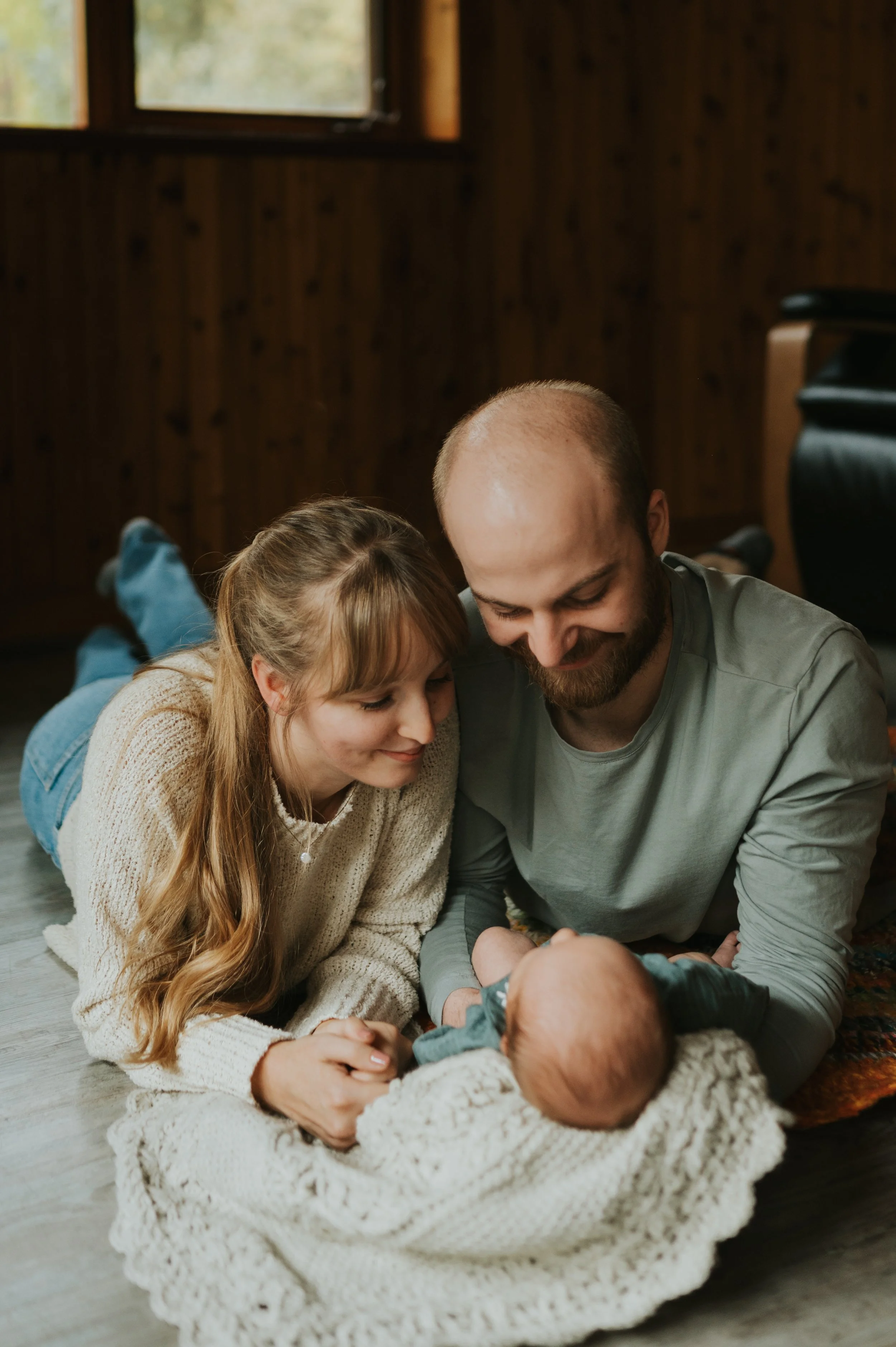 young couple smiles down at infant