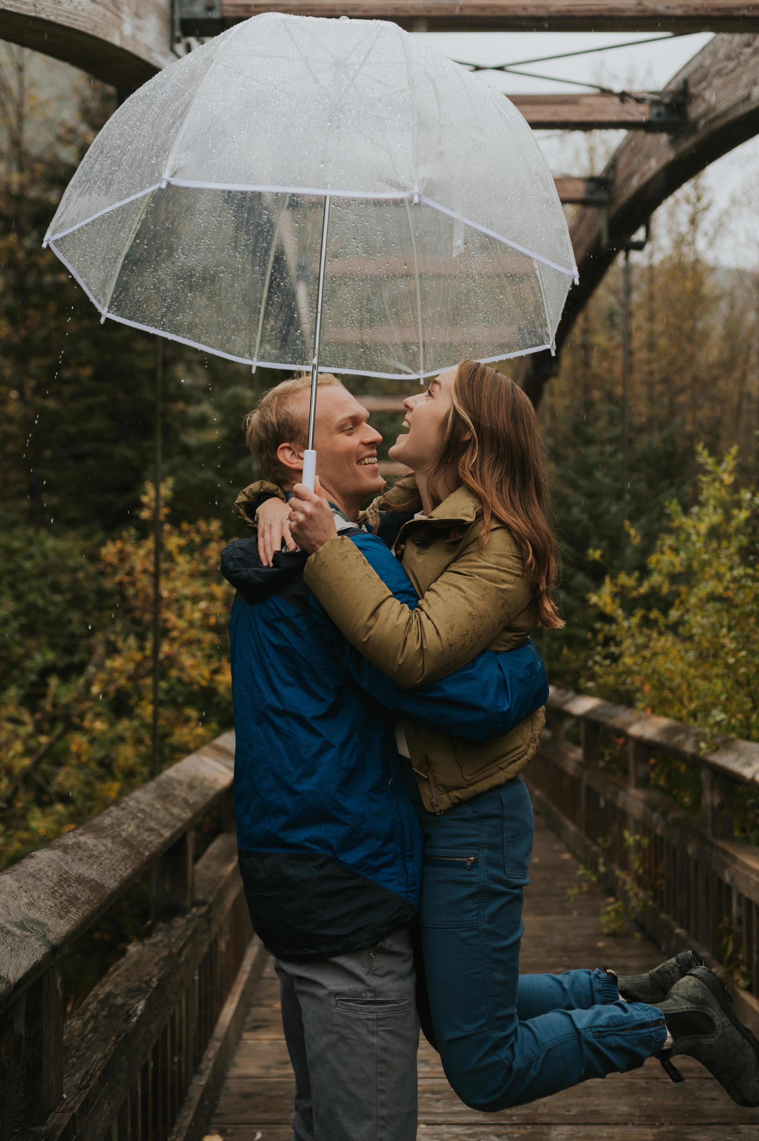 couple spinning in rain under clear umbrella