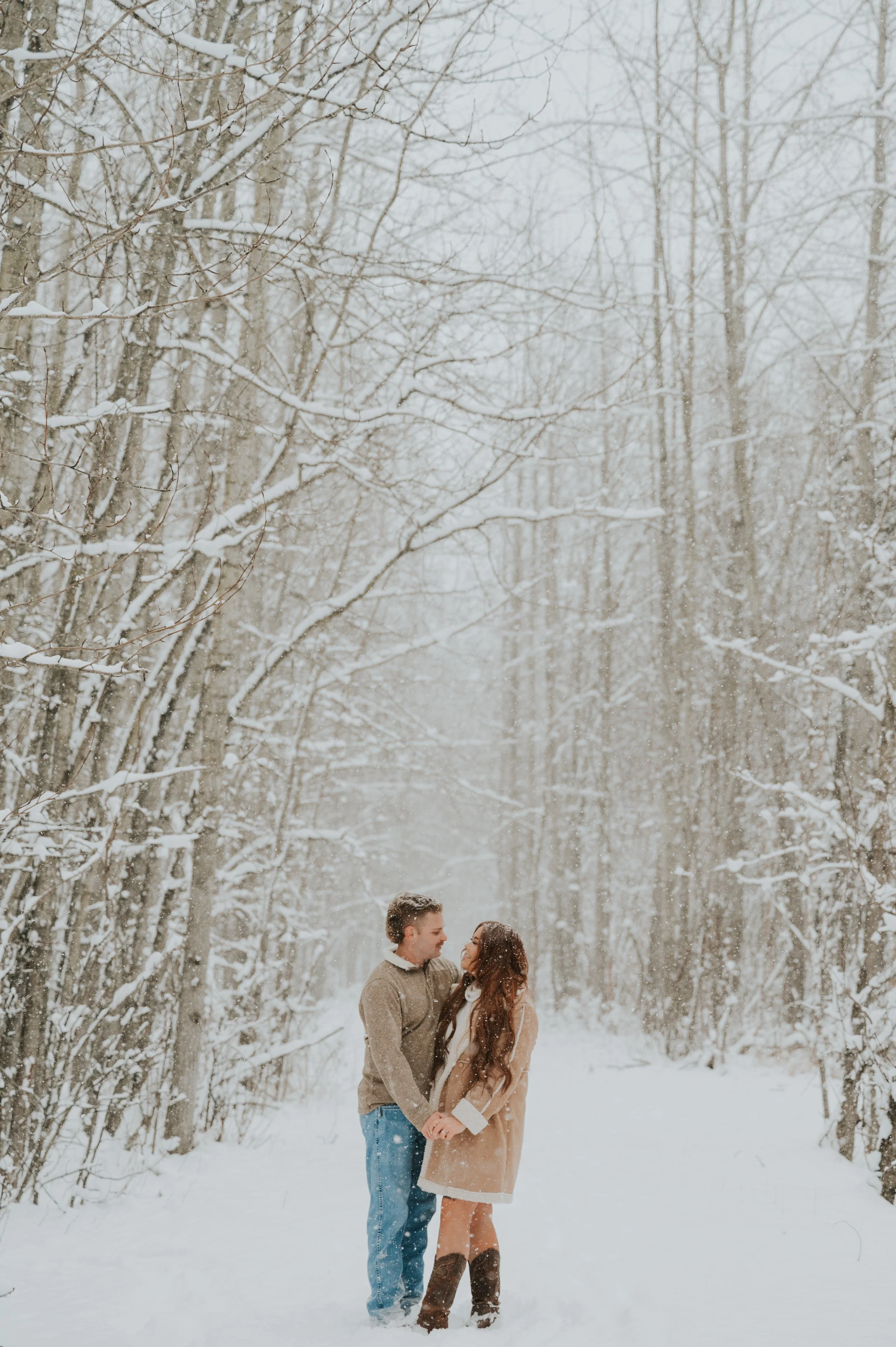 couple engaged and smiling at each other in snowy woods