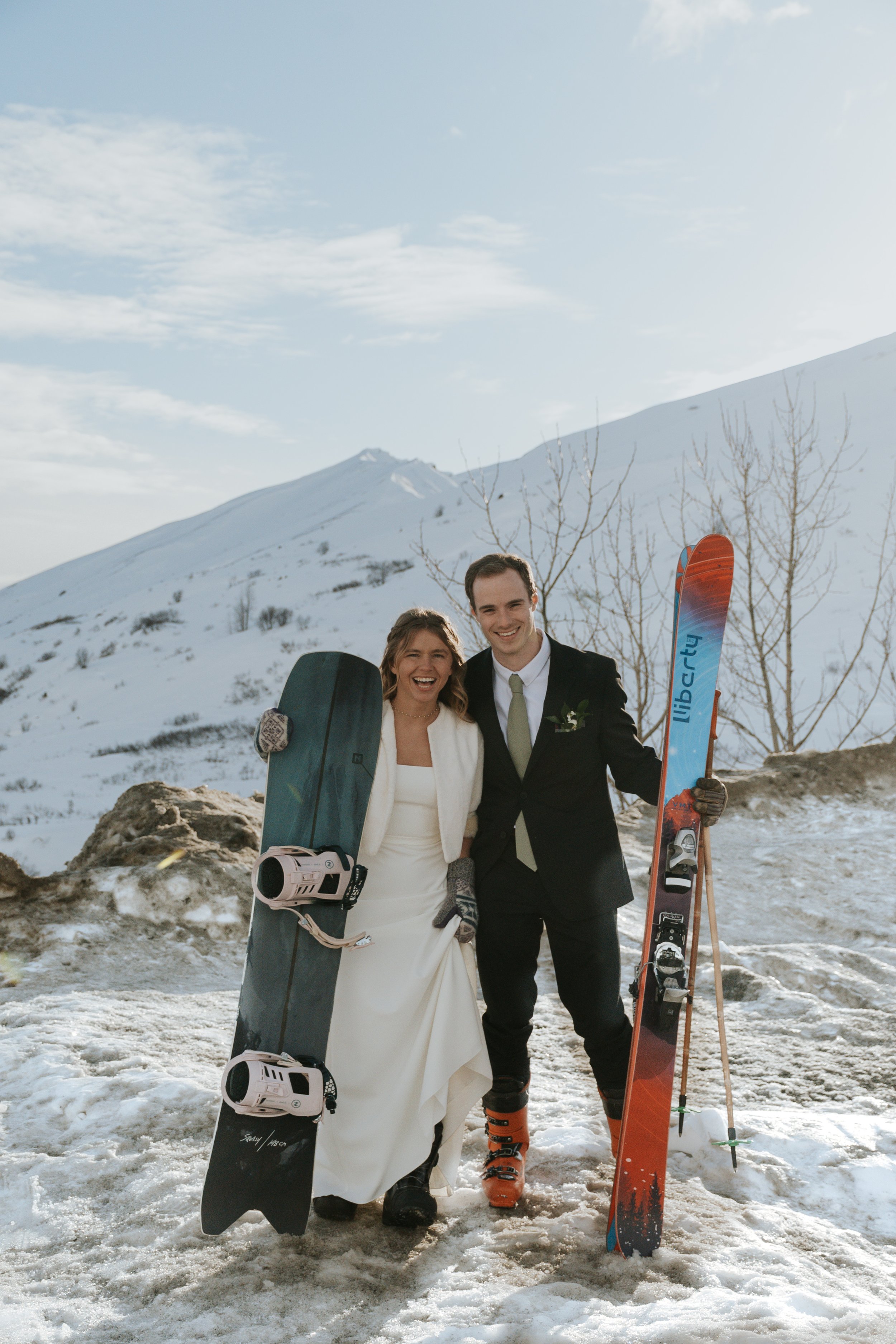 bride and groom in winter setting holding skis and snowboard