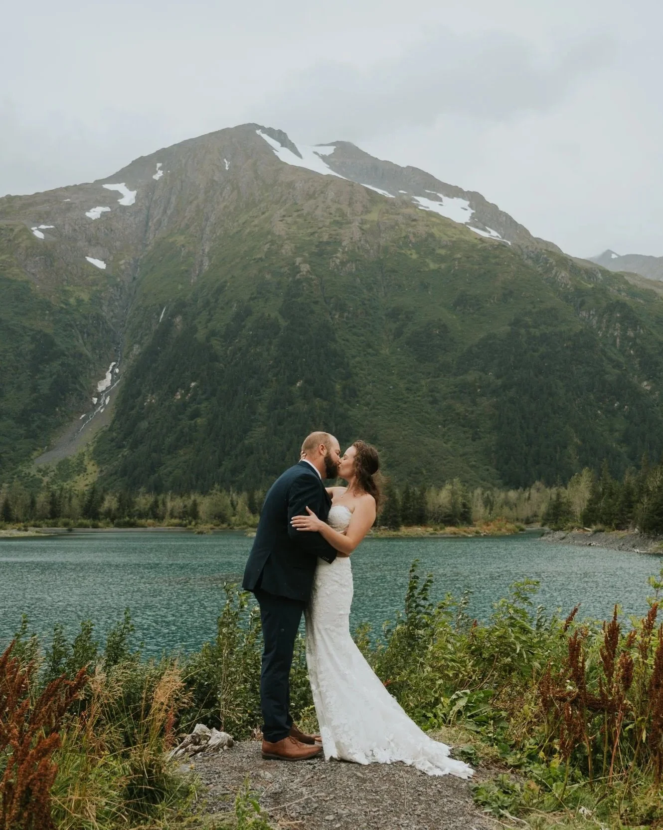 couple in wedding attire in front of alpine lake
