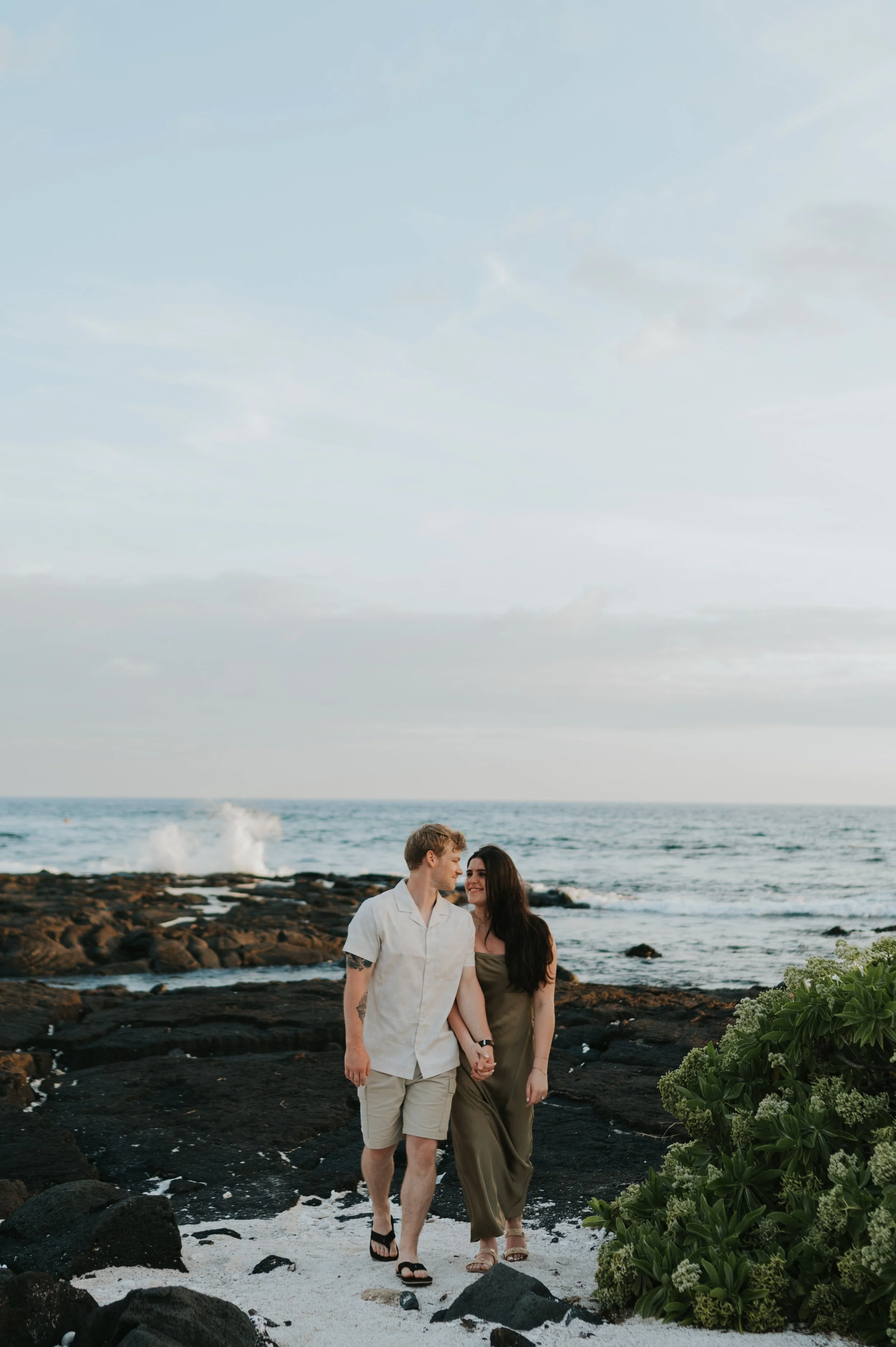 engaged couple walking towards camera holding hands on beach