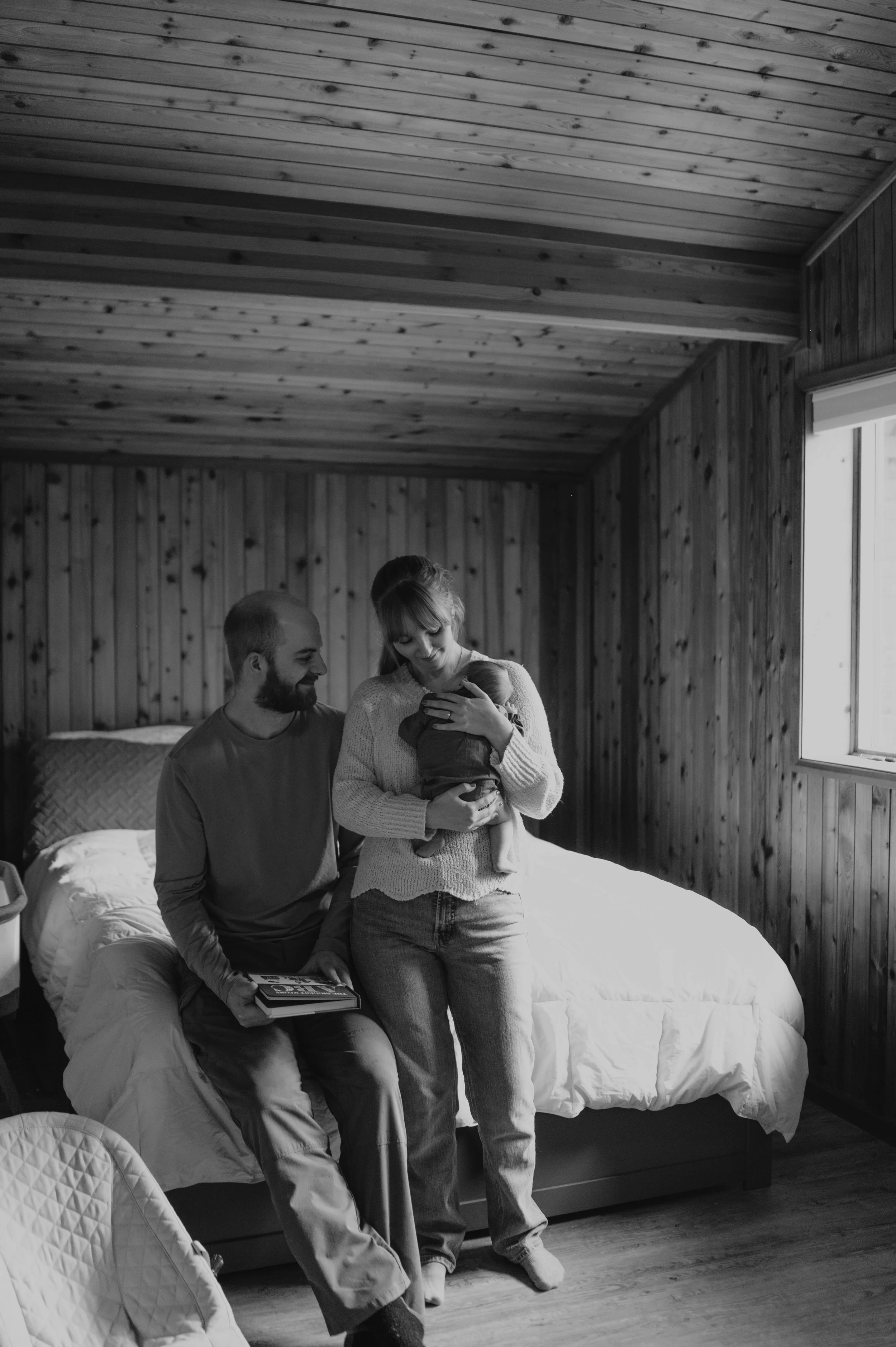mom holds infant while father smiles at them in bedroom