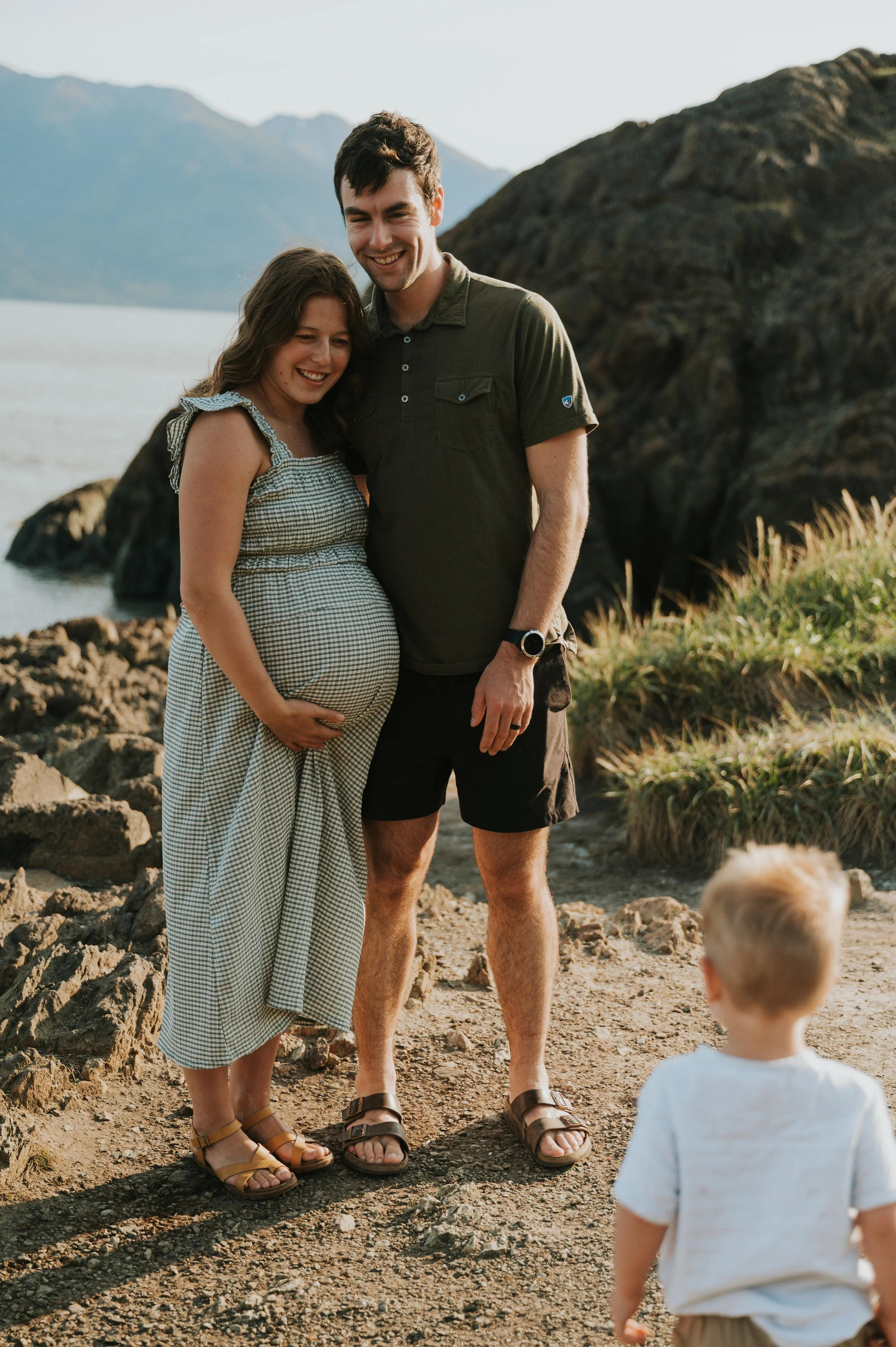 pregnant mom and husband smile at toddler