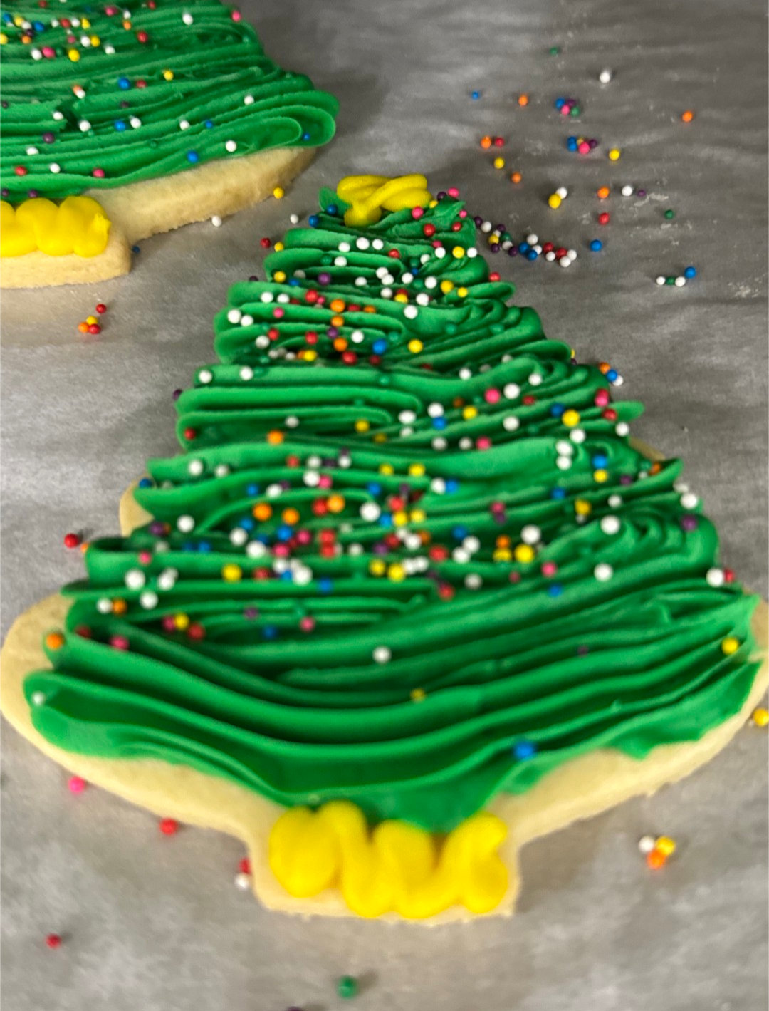 Christmas tree-shaped sugar cookies decorated with green and yellow icing and multicolored sprinkles.