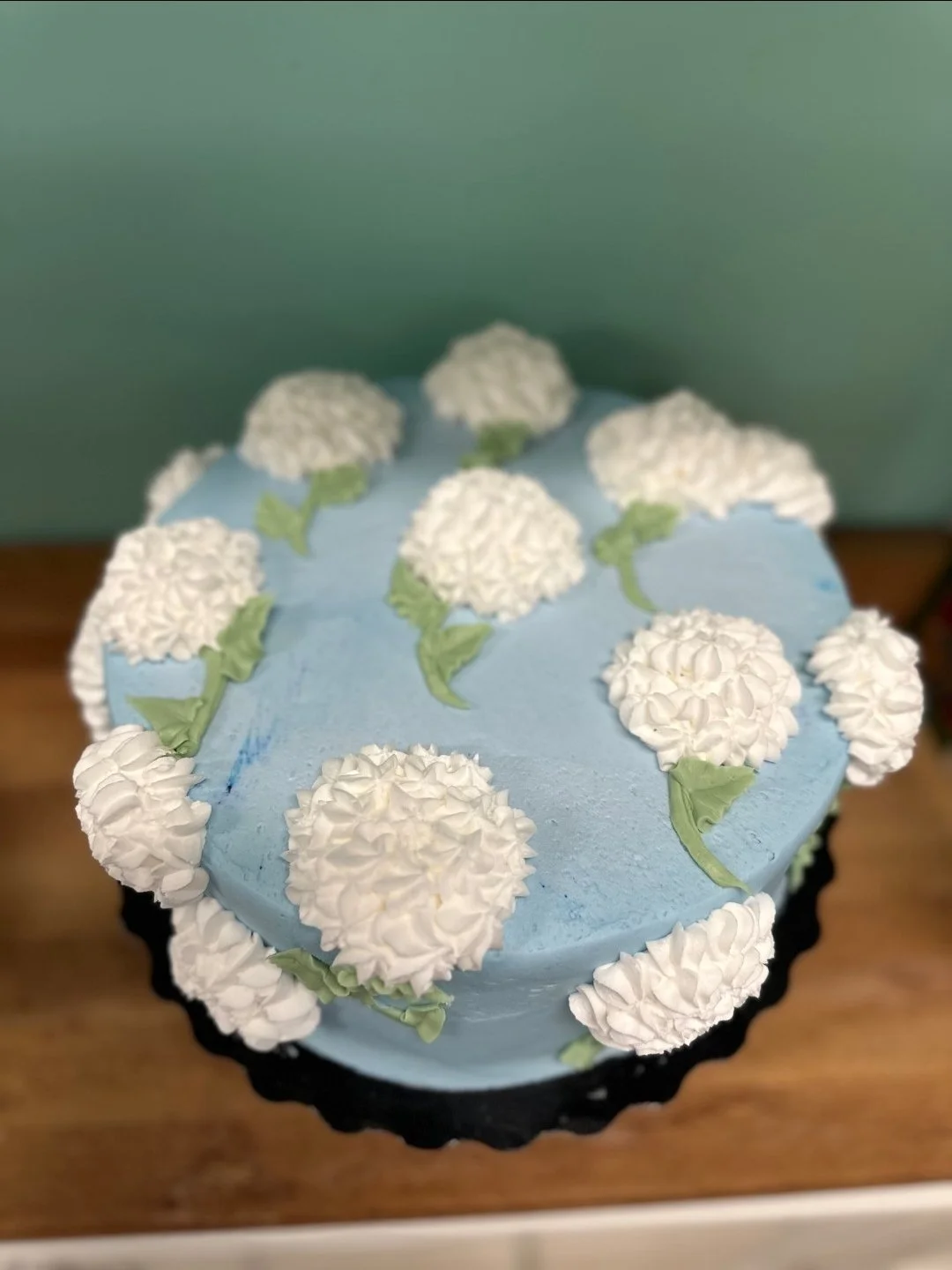 A cake decorated with white flowers and green leaves on a blue background.