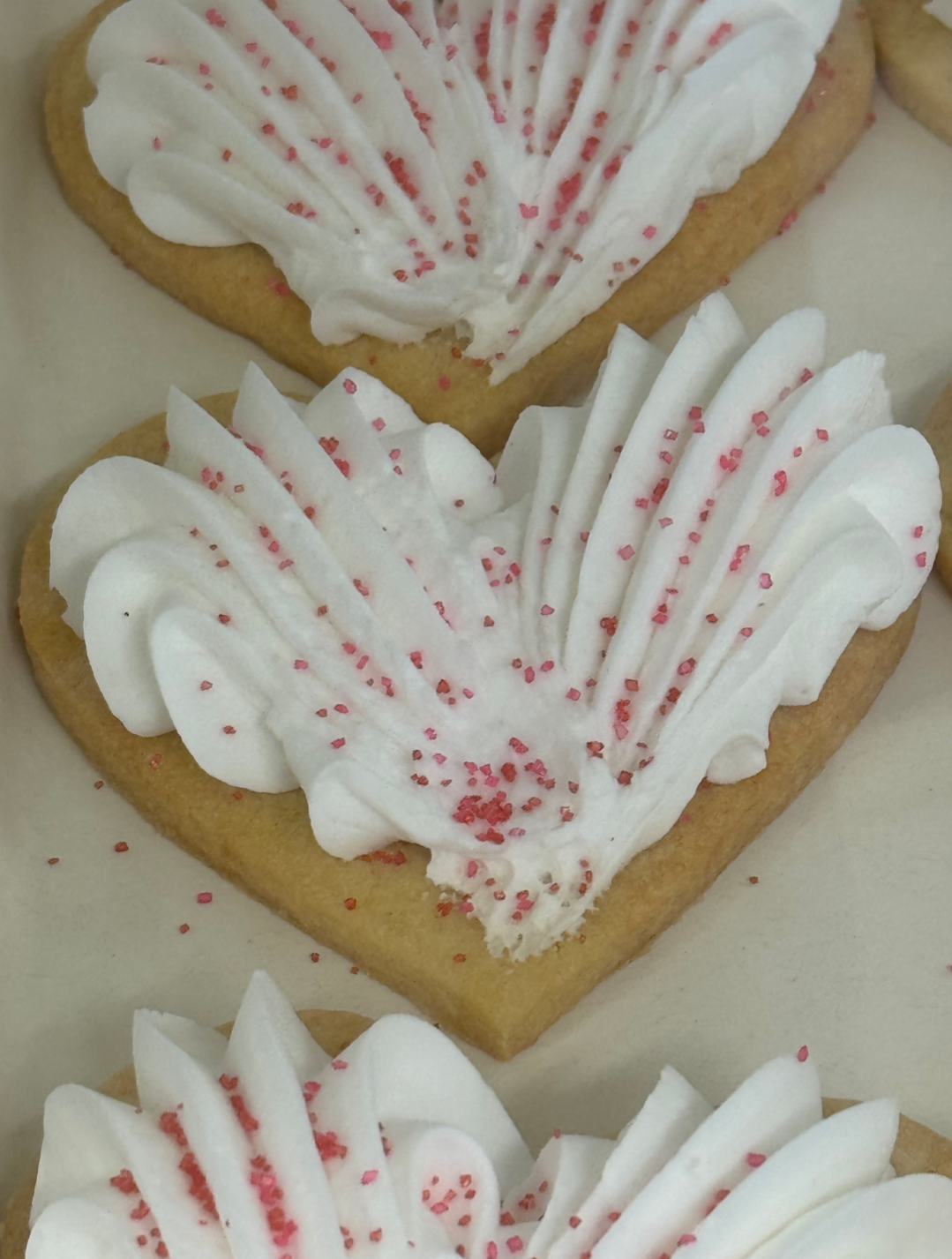 Heart-shaped sugar cookies decorated with white icing, piped frosting, and pink sprinkles