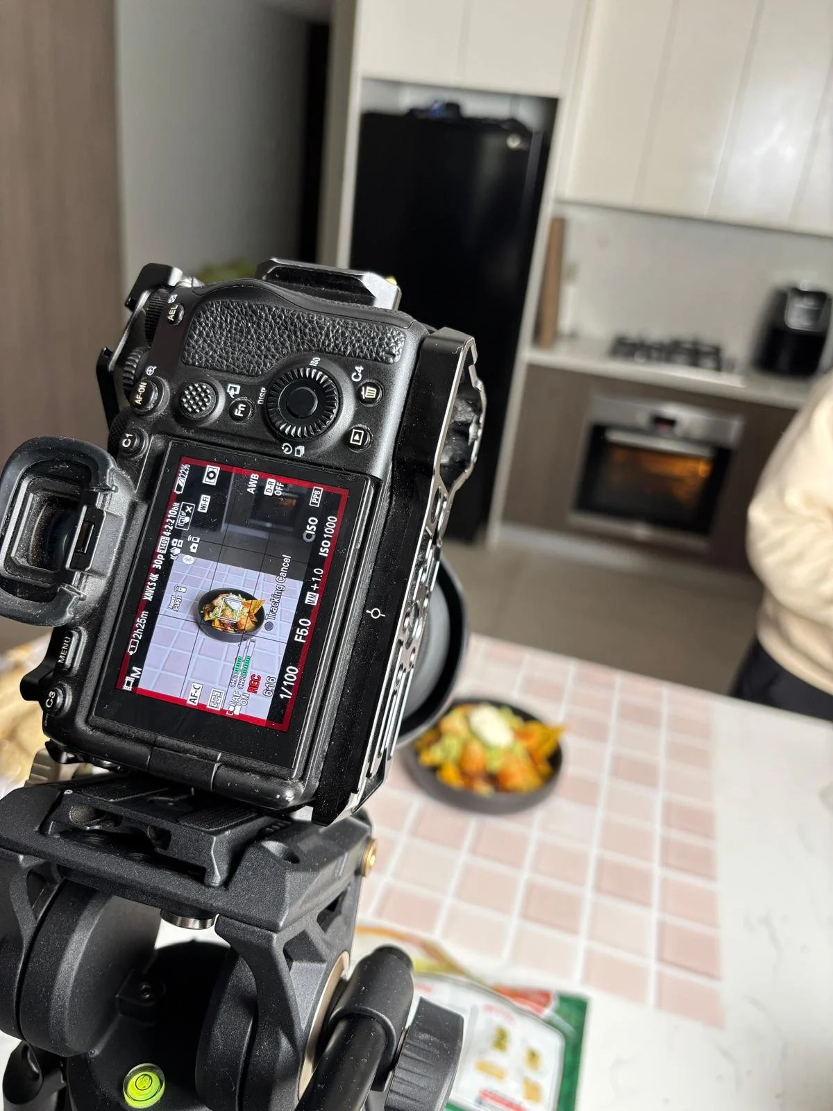 A digital camera taking a photo of a food dish on a tiled countertop in a kitchen.