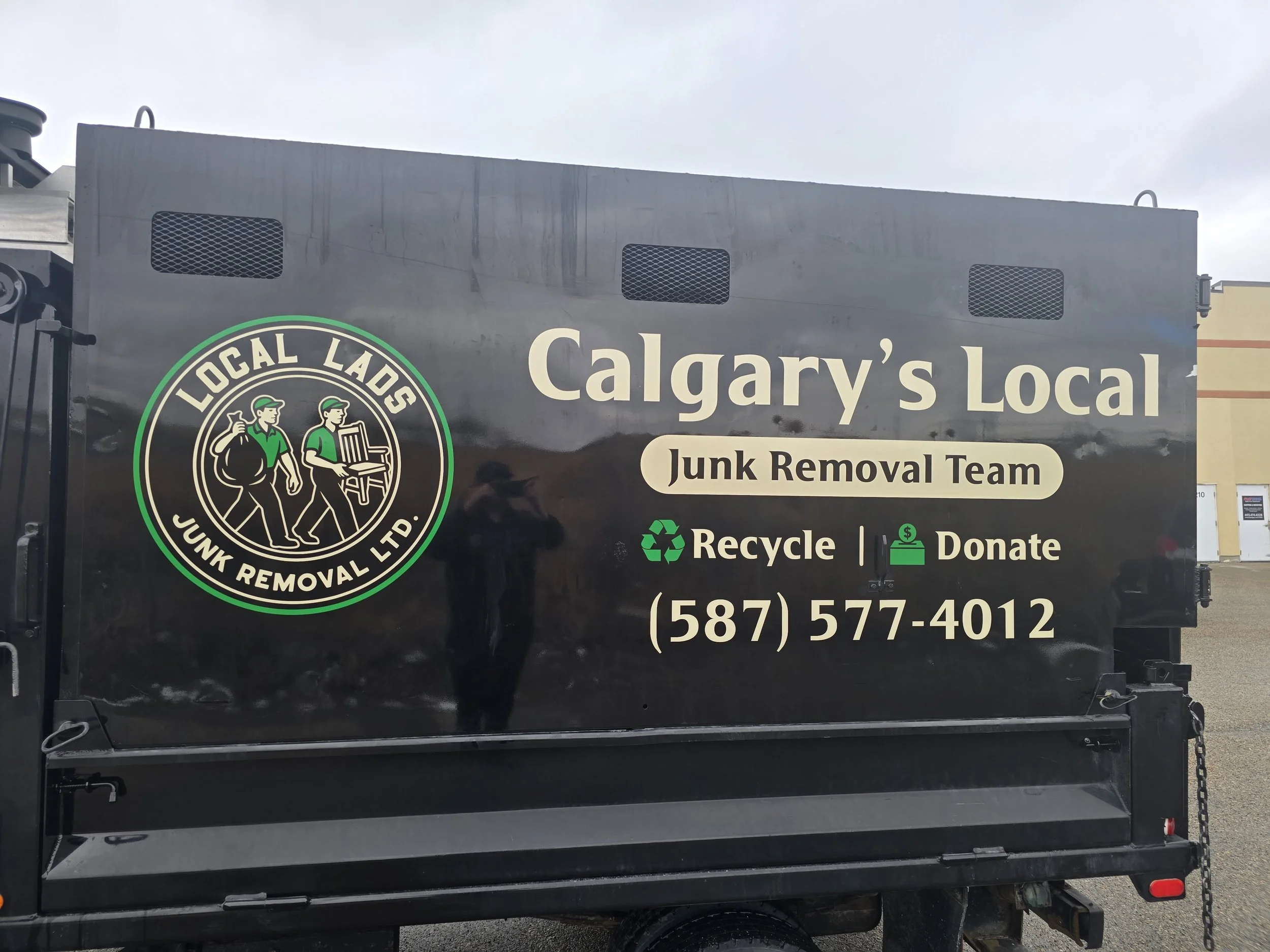 Black junk removal truck with green and white logo and text for Calgary's Local Junk Removal Team, including phone number (587) 577-4012, and icons for recycling and donation.