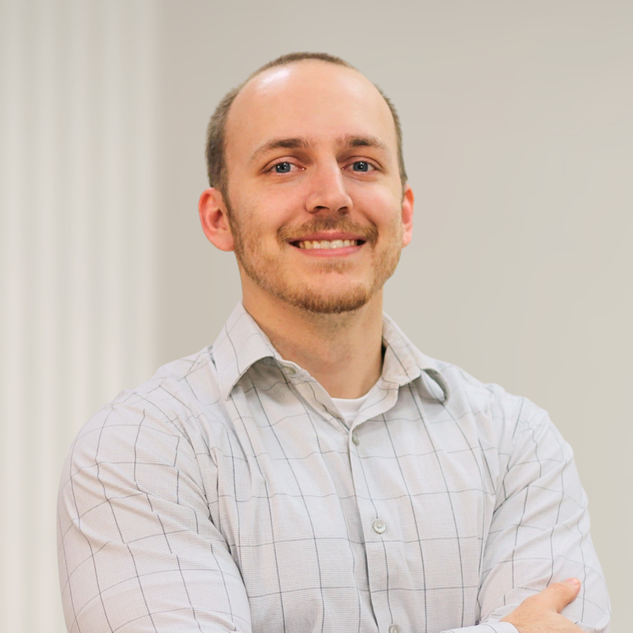 Portrait of a smiling man with a beard and short hair, wearing a dark green collared shirt, standing in front of a wooden decor background.