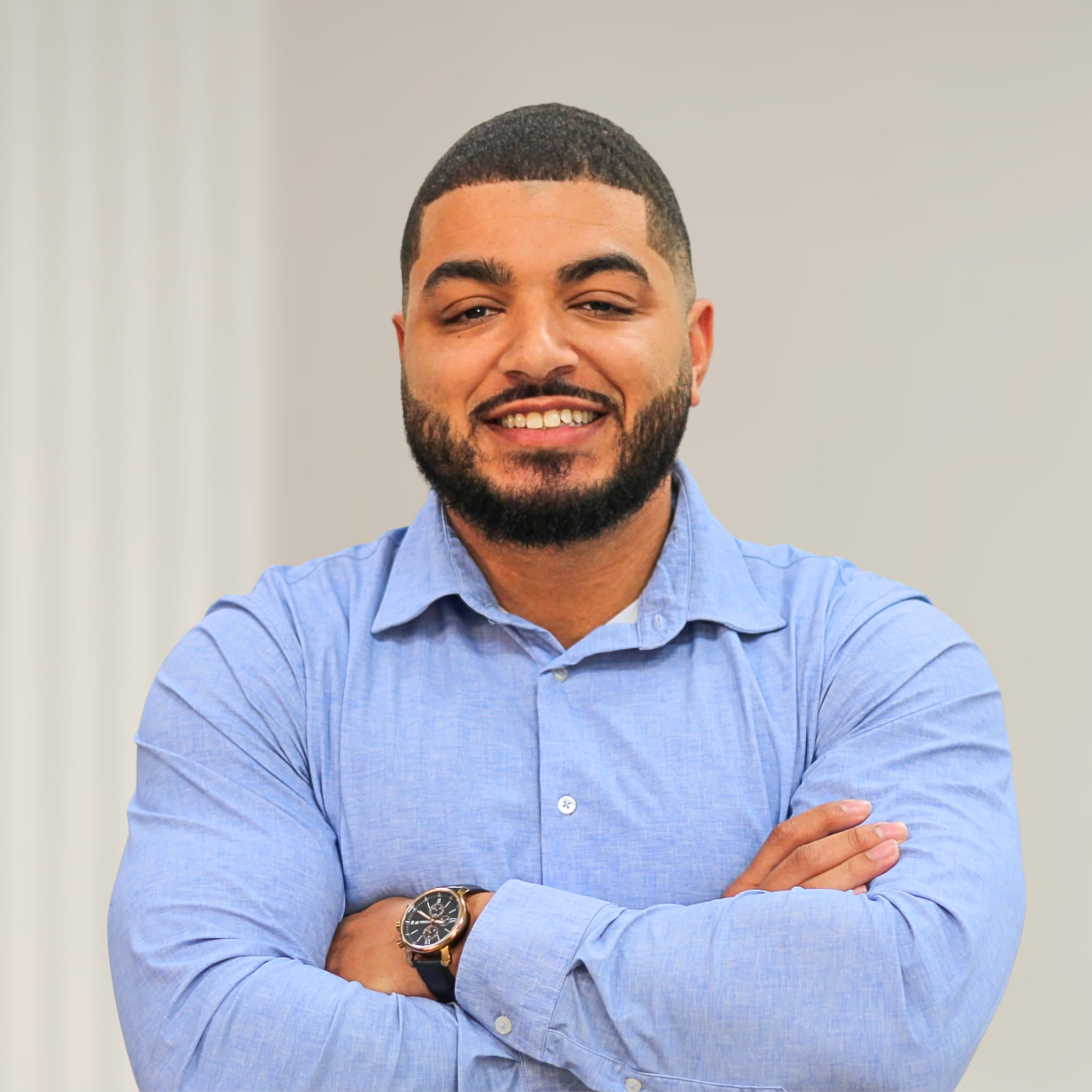 Confident man with crossed arms wearing a light blue button-up shirt standing in front of wooden slats.