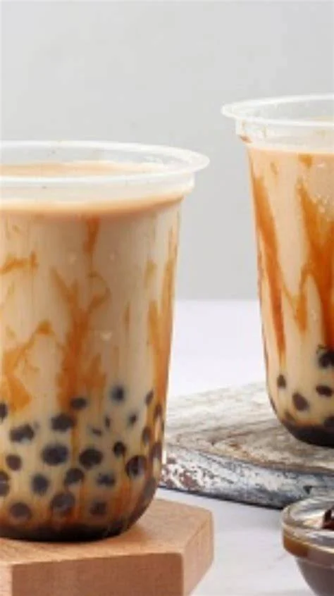 Two cups of bubble tea with tapioca pearls and caramel swirls on a wooden surface.
