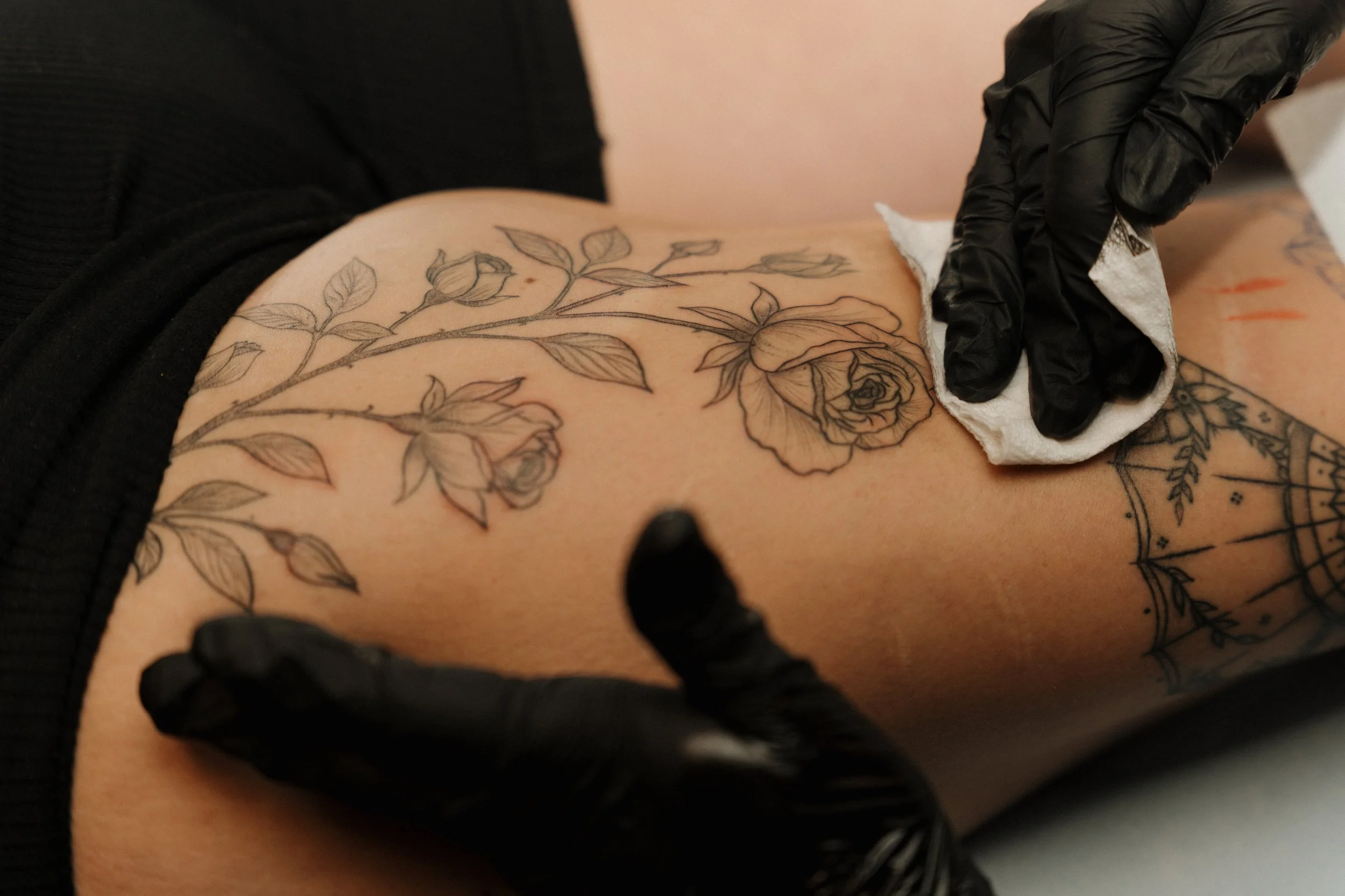 A person with black gloves is wiping a tattoo of roses  on their leg with a cloth.