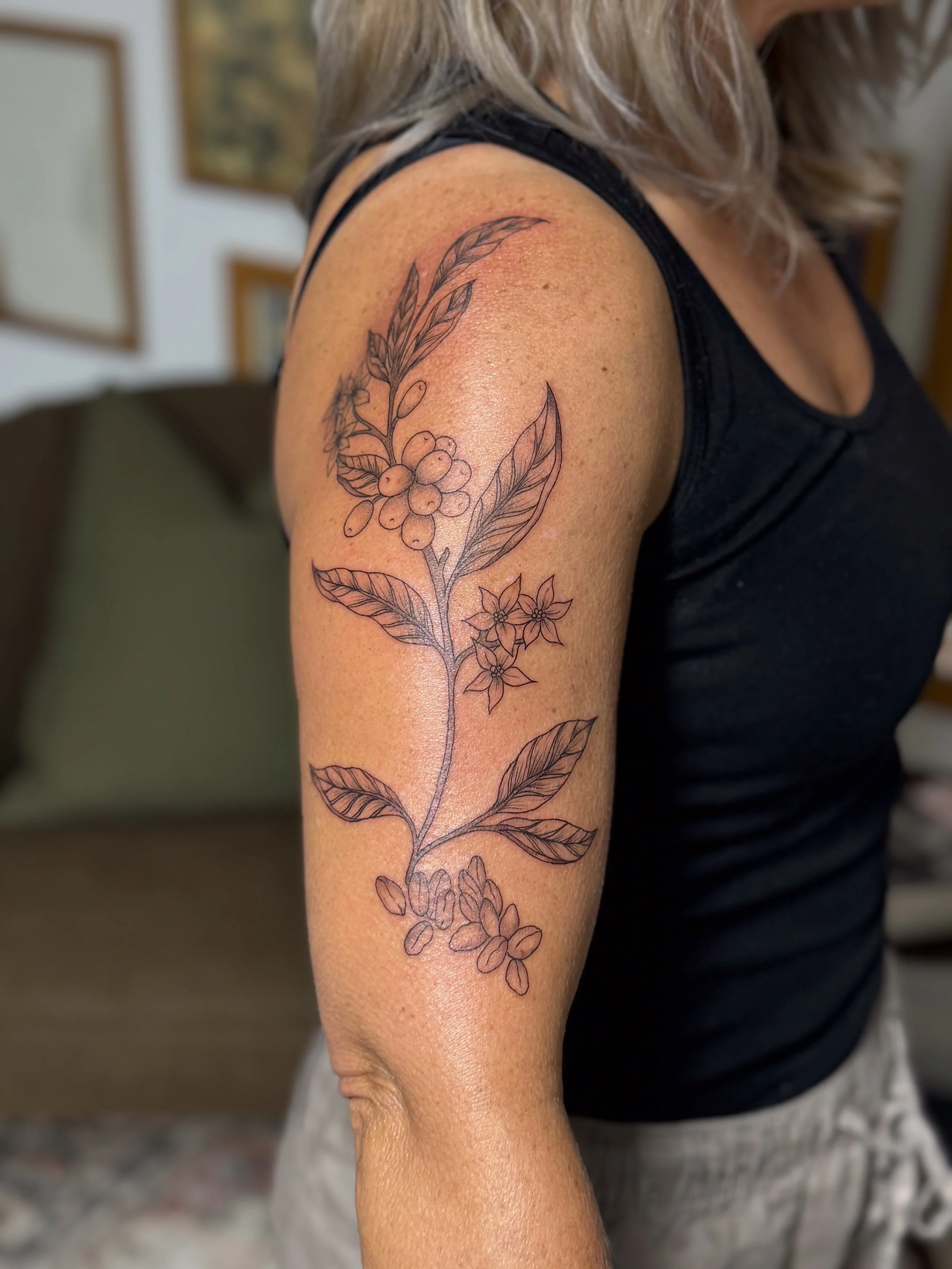 A woman's upper arm with a black outline floral tattoo design of leaves and berries.