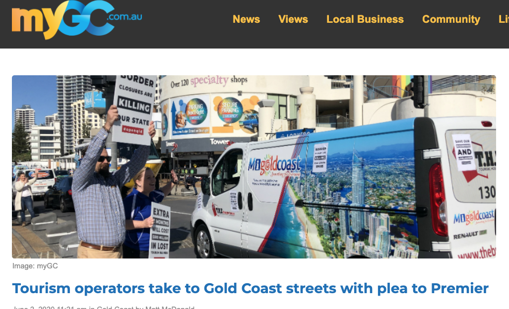 Protesters holding signs on a city street, with a van promoting Gold Coast tourism and buildings in the background.