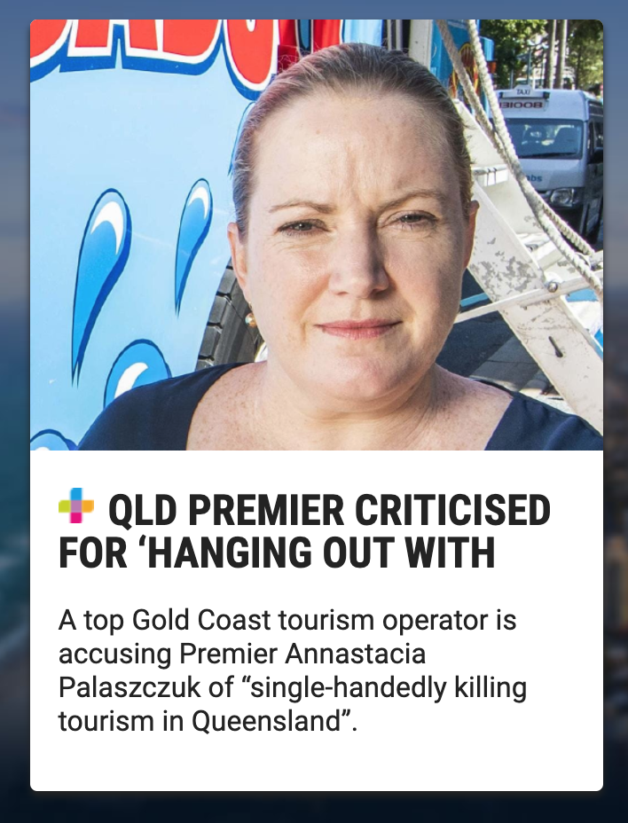 A close-up of a woman outdoors, with a blue tour bus in the background and some trees and vehicles visible. She has her hair pulled back and is wearing earrings.