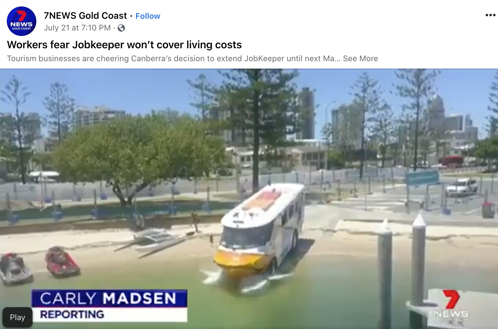 A boat is sinking into the water at a marina or harbor, with the bow submerged and water splashing around it. Other boats are docked nearby, and there are trees, buildings, and parking lot in the background.