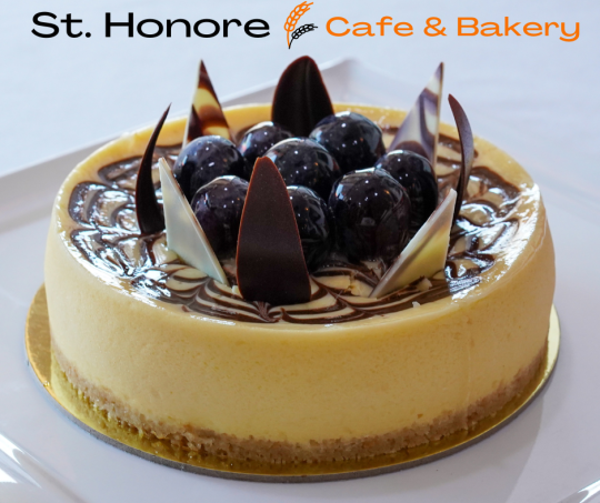 Cheesecake topped with blueberries and decorative chocolate pieces, with a St. Honore Cafe & Bakery logo.