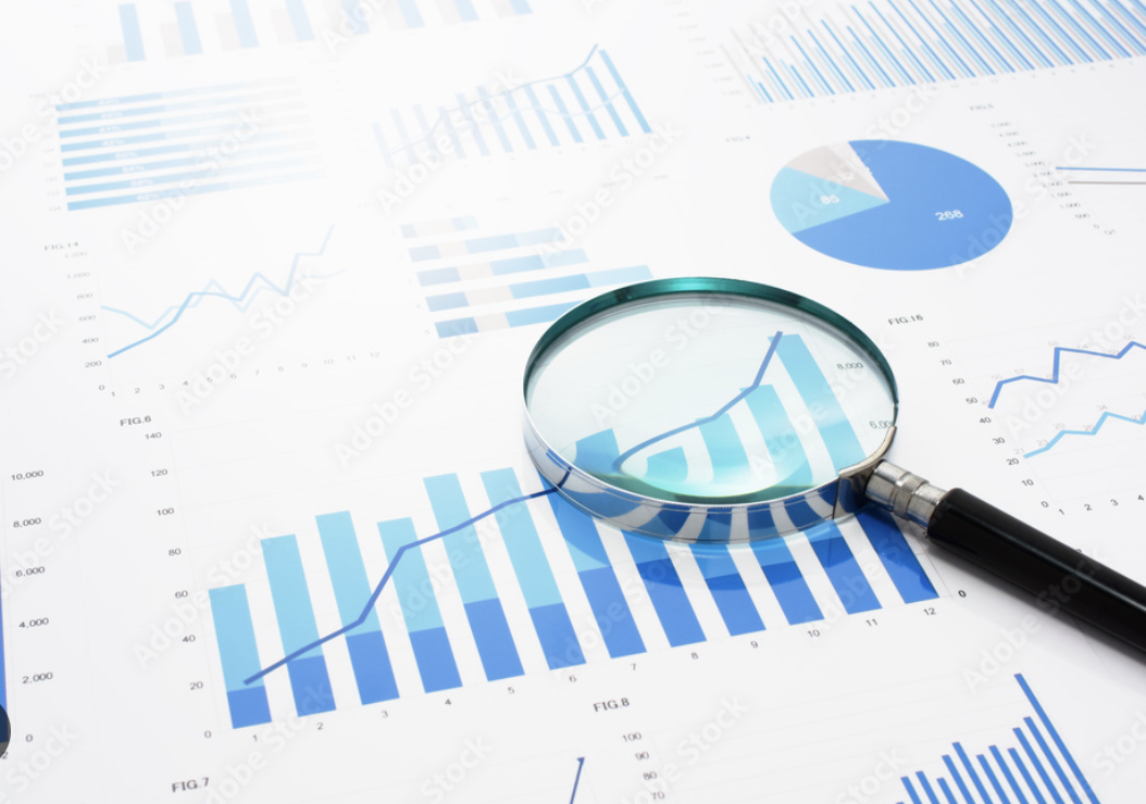 Financial charts and graphs on paper shown alongside a magnifying glass focusing on a line and bar graph.