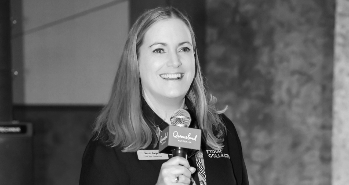 A woman smiling while holding a microphone with a sign that reads 'Queensland Australia'.