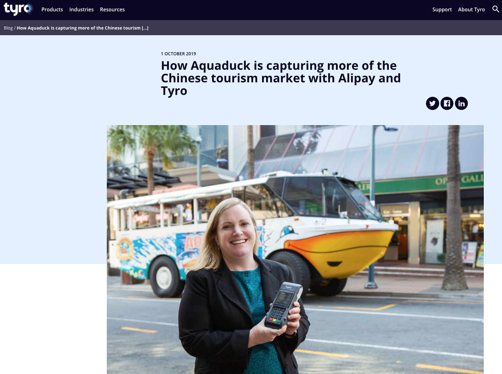 A woman standing on a city street holding a mobile point of sale device, with a colorful tour bus and tall palm trees in the background.
