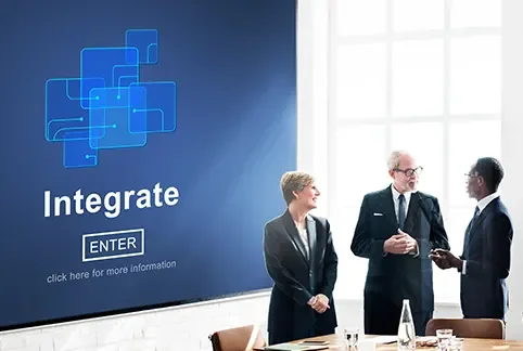 Three business professionals in a meeting room, two women and one man, engaged in conversation with a large screen displaying digital graphics and the word 'Integrate' and an 'ENTER' button.