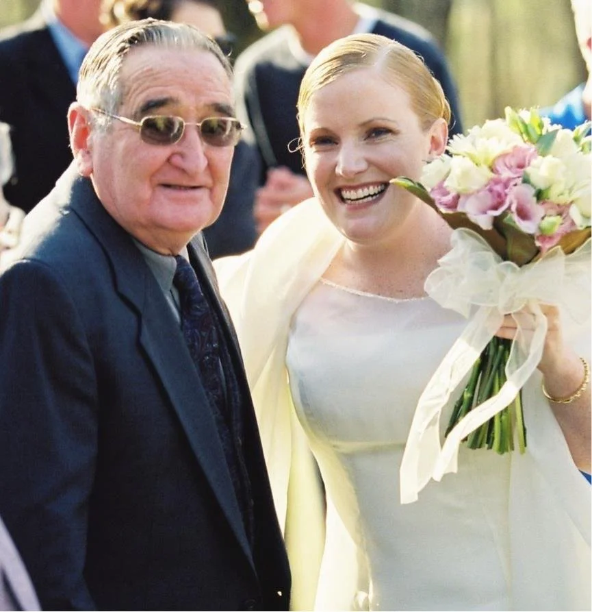 A woman holding a bouquet of flowers smiling with an older man at an outdoor event.