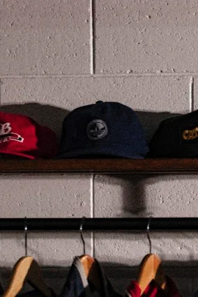 Three baseball caps on a wooden shelf, with a brick wall in the background.
