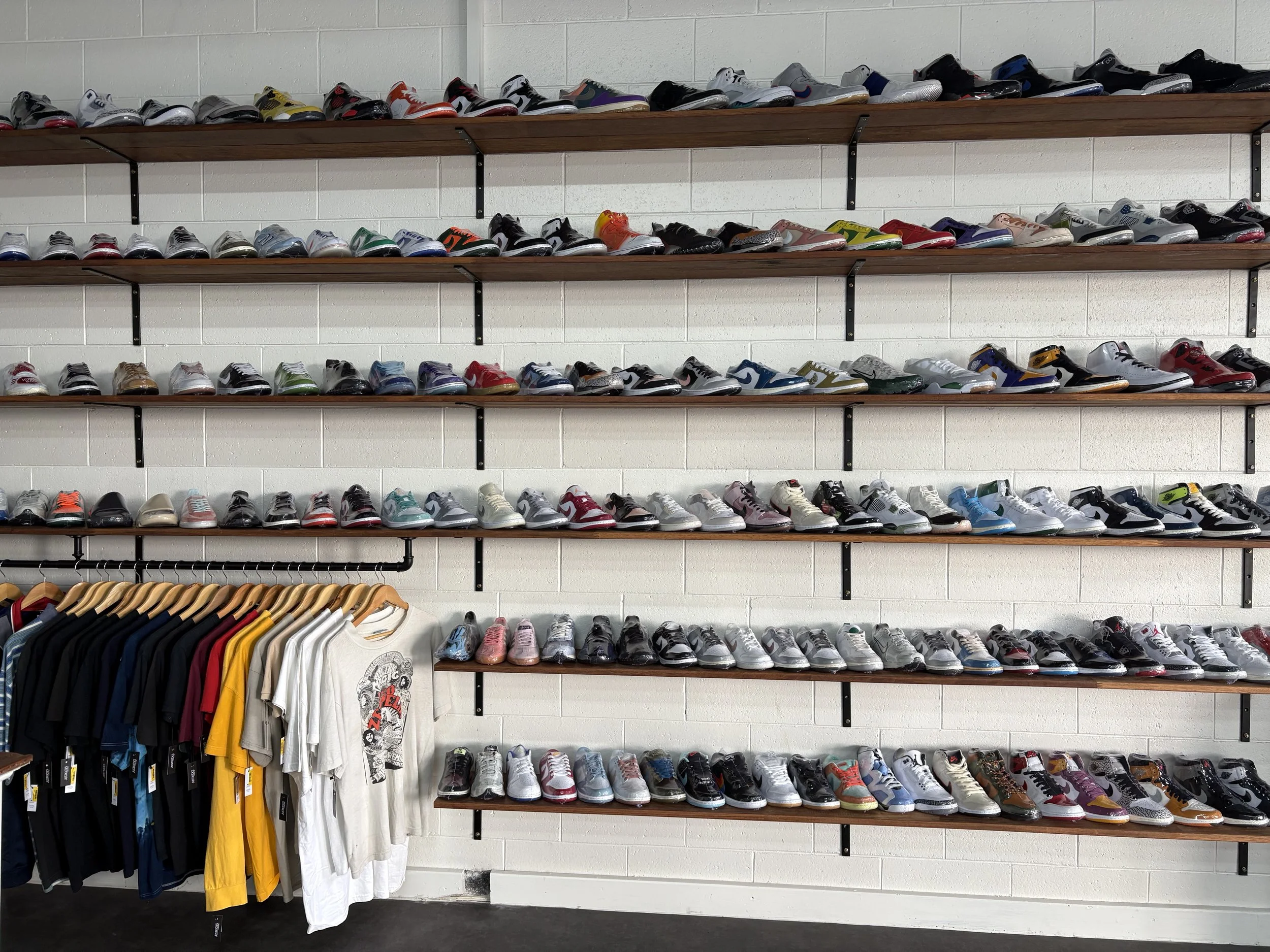 Display of athletic shoes on wooden shelves and T-shirts hanging on a rack at a retail store.