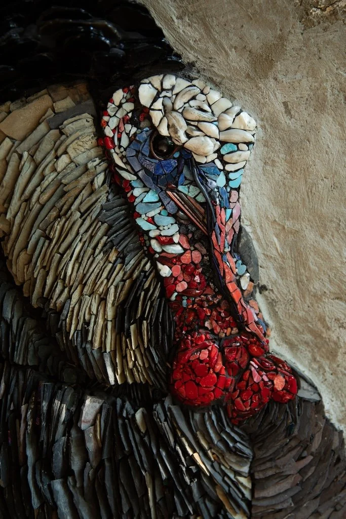 Mosaic art of a bird, the American wild turkey, made from colored stones and tiles, placed on a rock surface.