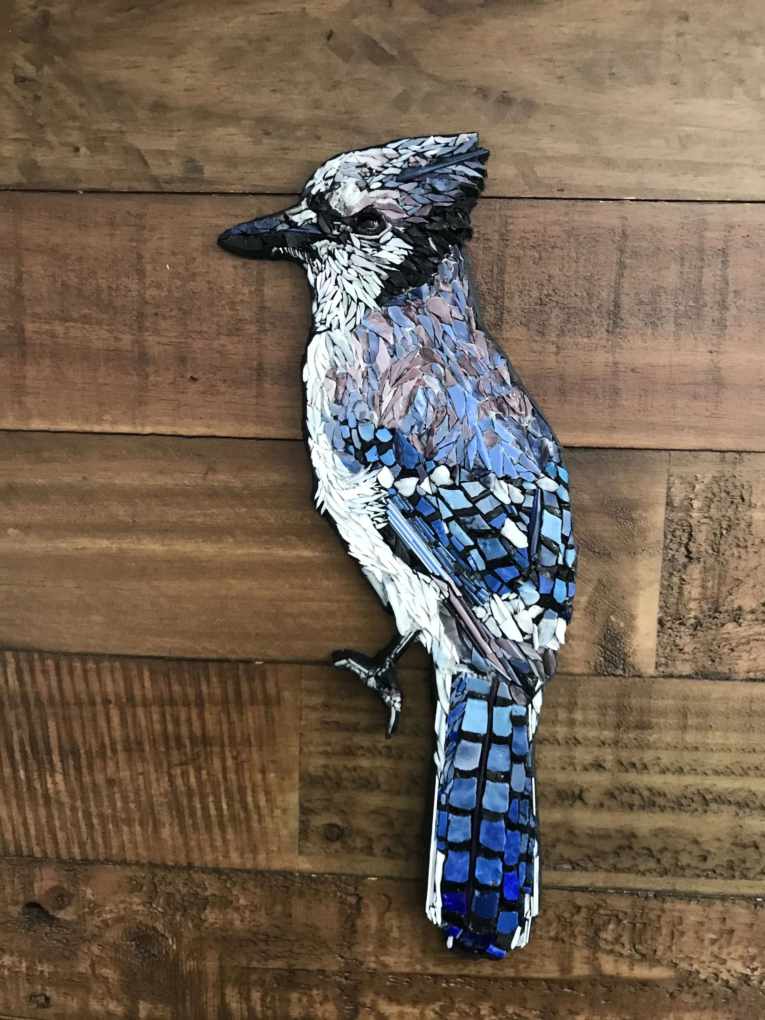 Mosaic art of a blue jay bird on a wooden wall background.