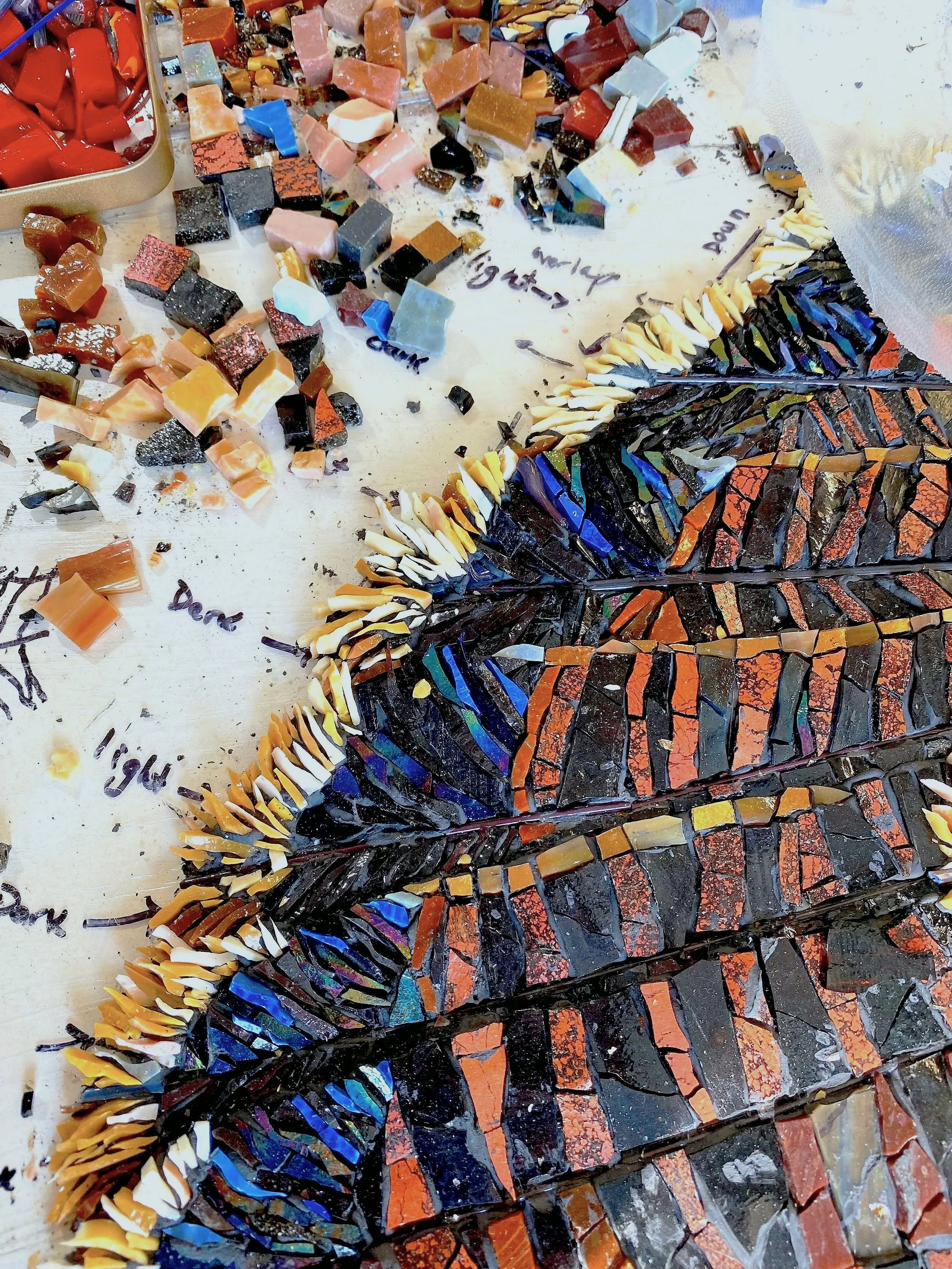 Colorful mosaic stained glass panels arranged in a diagonal pattern with loose mosaic pieces scattered around.