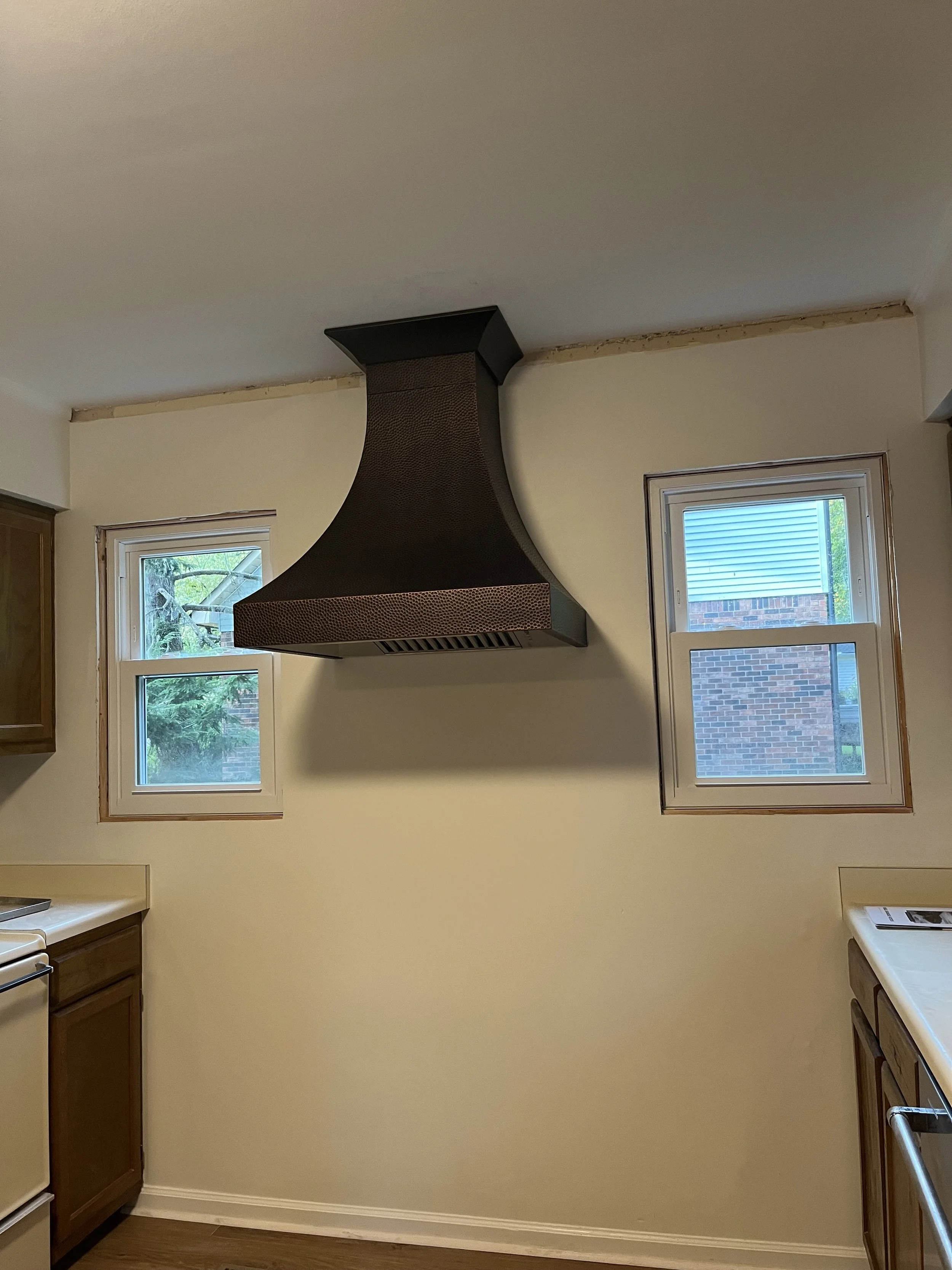 An image of a beautiful copper range hood between two windows