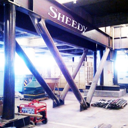 Industrial interior with large metallic structure labeled ‘SHEEDY’, construction tools, and equipment on the floor.
